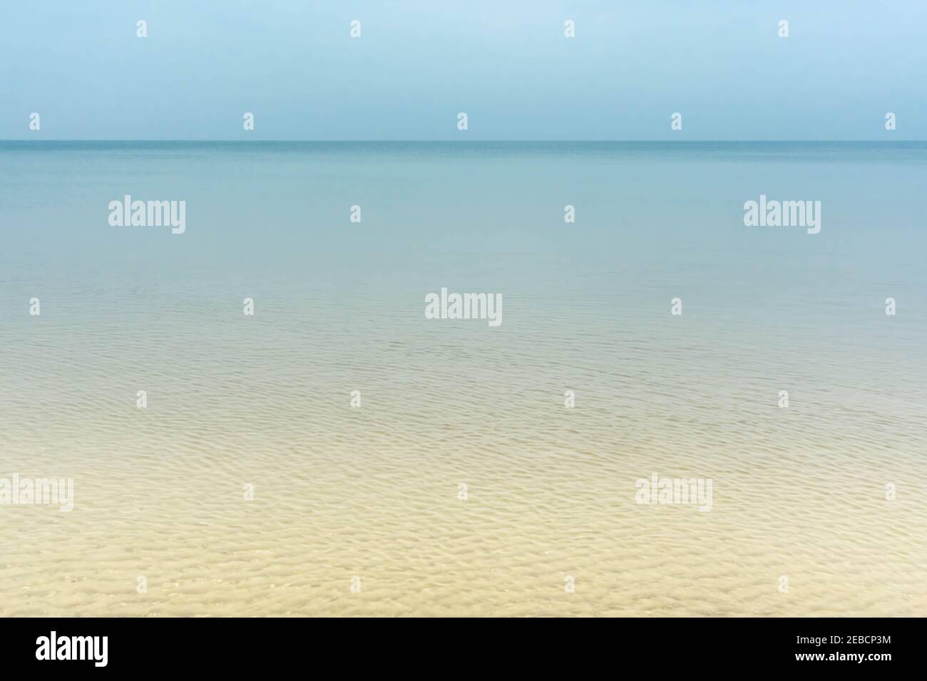 Beigefarbener Sandstrand und türkisfarbener, gewellter Meereshintergrund. Transparentes blaues Meerwasser über Sandstrand. Glänzendes, winkendes Meerwasser über dem Sandstrand. Summert Stockfoto