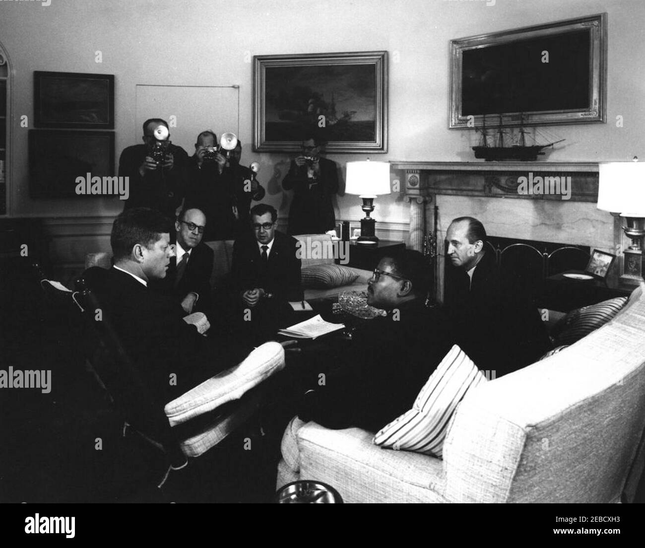 Treffen mit dem Botschafter von Gabun, Jules Mbah, 11:48am. Präsident John F. Kennedy (sitzt in Schaukelstuhl) trifft sich mit dem Botschafter von Gabun, Jules Mbah. L-R: Präsident Kennedy; stellvertretender Direktor des Büros für westafrikanische und madagassische Angelegenheiten Donald Dumont; Dolmetscher Josu00e9 de Seabra; Botschafter Mbah; Protokollchef Angier Biddle Duke. Fotografen stehen zurück. Oval Office, White House, Washington, D.C. Stockfoto