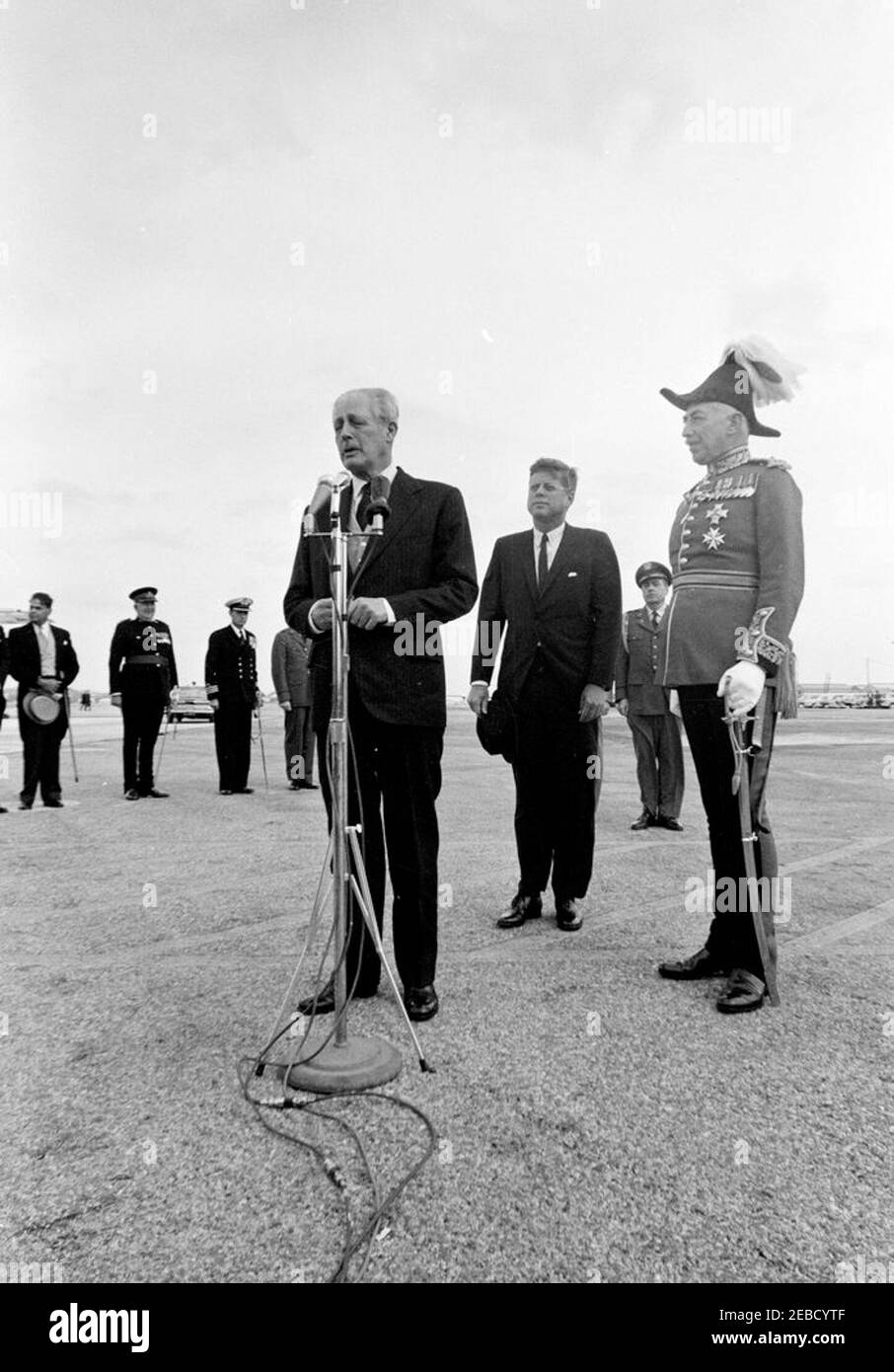 Reise nach Bermuda: Ankunft auf der Kindley Air Force Base, Bermuda, 12:55pm Uhr. Premierminister von Großbritannien Harold Macmillan spricht die Menschenmenge über Präsident John F. Kennedyu2019s Ankunft in Bermuda von Palm Beach, Florida. Präsident Kennedy und der Gouverneur von Bermuda, Generalmajor Sir Julian Gascoigne, stehen auf der rechten Seite. Air Force Aide to the President Brigadier General Godfrey T. McHugh steht im Hintergrund zwischen dem Präsidenten und Gouverneur Gascoigne. Alle anderen sind nicht identifiziert. Kindley Air Force Base, St. Davidu2019s Island, Bermuda. Stockfoto