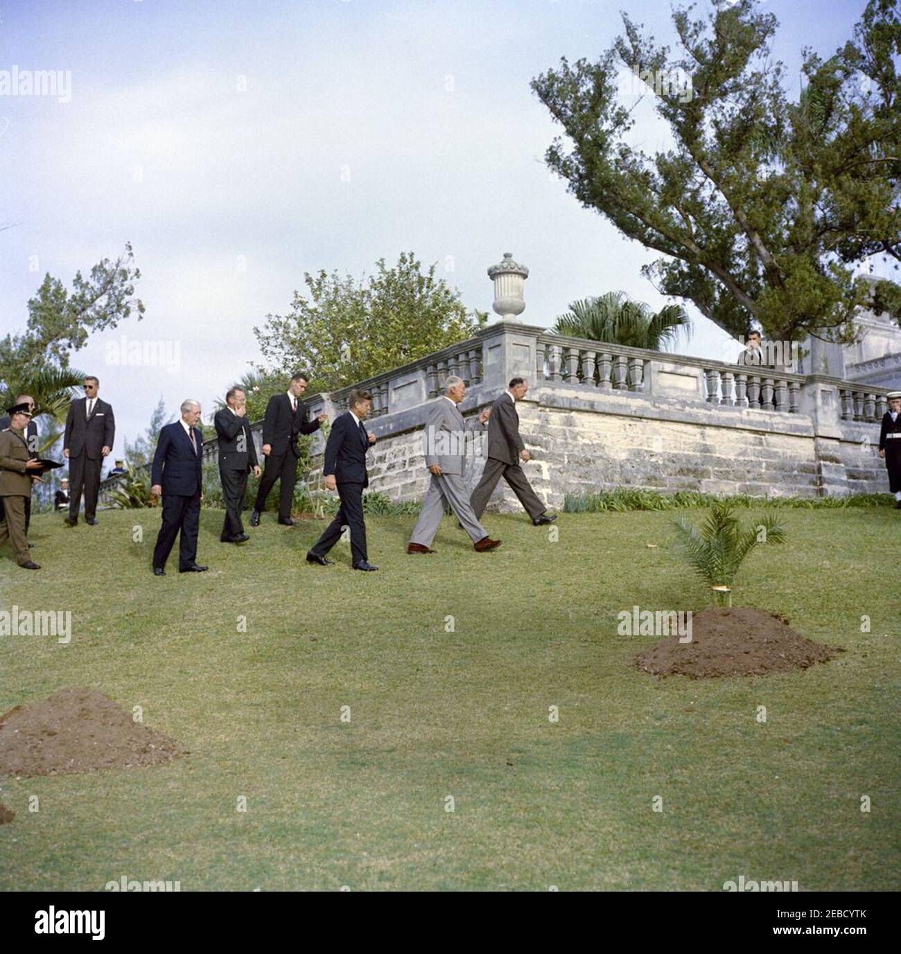 Ausflug nach Bermuda: Baumpflanzung im Government House, Hamilton, Bermuda. Präsident John F. Kennedy und andere gehen auf dem Gelände des Government House in Hamilton, Bermuda. L-R: Nicht identifiziert; Geheimagenten des Weißen Hauses Ernest u201cErnieu201d Olsson (hinter unidentifizierten Mann) und Arthur L. u201cArtu201d Godfrey; Premierminister von Großbritannien Harold Macmillan; Präsident Kennedyu2019s Sonderassistent für nationale Sicherheit McGeorge Bundy; Geheimagenten des Weißen Hauses William L. u201cBillu201d Duncan; Präsident Kennedy; Gouverneur von Bermuda Generalmajor Sir Julian Gasc Stockfoto