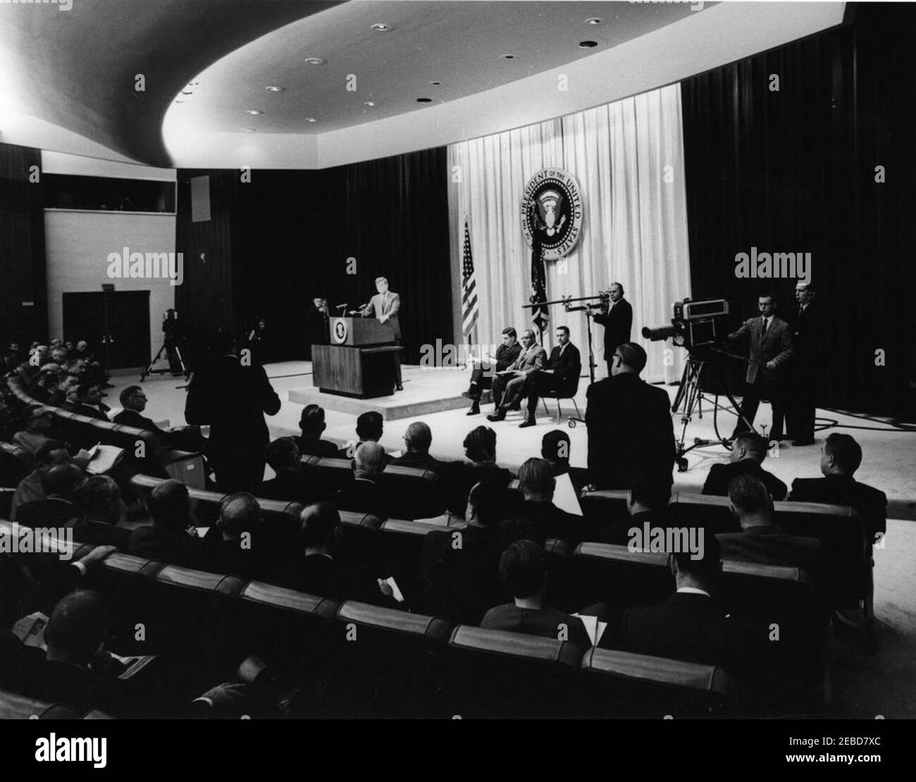 Pressekonferenz, State Department Auditorium, 10:00am Uhr. Präsident John F. Kennedy hört zu, wie ein Reporter eine Frage an einer Pressekonferenz stellt, die im Auditorium des Außenministeriums in Washington, D.C. abgehalten wird. Sitzen auf der Bühne sind (L-R): White House Press Secretary Pierre Salinger, Associate White House Press Secretary Andrew Hatcher und Assistant White House Press Secretary Jay Gildner. Stockfoto Pressekonferenz, State Department Auditorium, 10:00am Uhr. Präsident John F. Kennedy hört zu, wie ein Reporter eine Frage an einer Pressekonferenz stellt, die im Auditorium des Außenministeriums in Washington, D.C. abgehalten wird. Sitzen auf der Bühne sind (L-R): White House Press Secretary Pierre Salinger, Associate White House Press Secretary Andrew Hatcher und Assistant White House Press Secretary Jay Gildner. Stockfoto