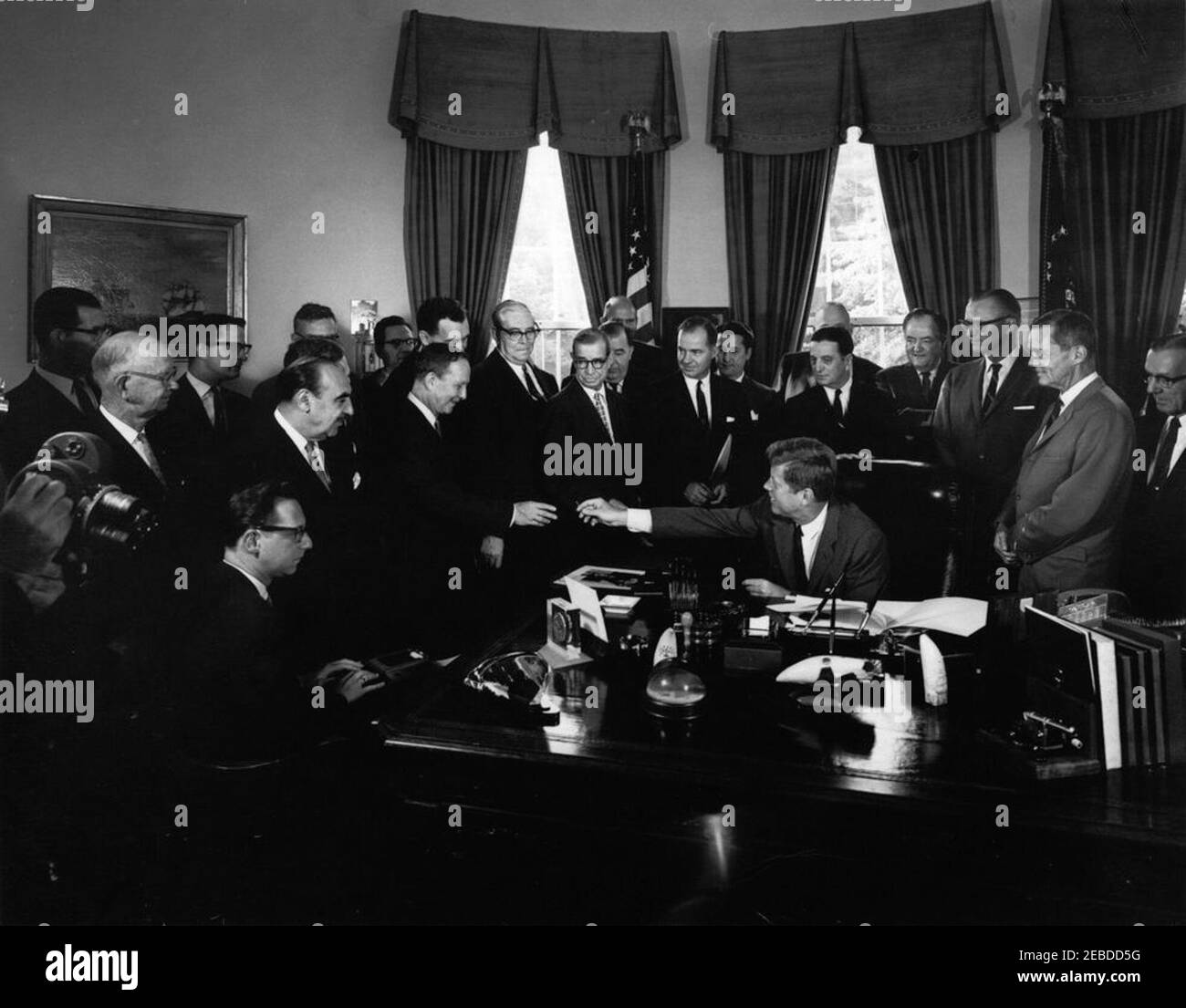 Bill Signing - S. 2965 Öffentliches Recht 87658, Accelerated Public Works Program, 9:30am. Präsident John F. Kennedy (am Schreibtisch sitzend) reicht Senator Stephen M. Young (Ohio) nach der Unterzeichnung von S. 2965, dem Public Works Acceleration Act, einen Stift. Von links nach rechts: Nicht identifizierter Stenograf (sitzend); Senator Oren E. Long (Hawaii); zwei nicht identifizierte (hinten); Sekretär des Ministeriums für Gesundheit, Bildung und Wohlfahrt (HEW), Anthony J. Celebrezze; zwei nicht identifizierte (hinten); Senator Young (vom Präsidenten Kennedy empfangen); Senator Edmund S. Muskie (Maine); Senator Pat McNamara (Michigan); Senator Dennis C. Stockfoto