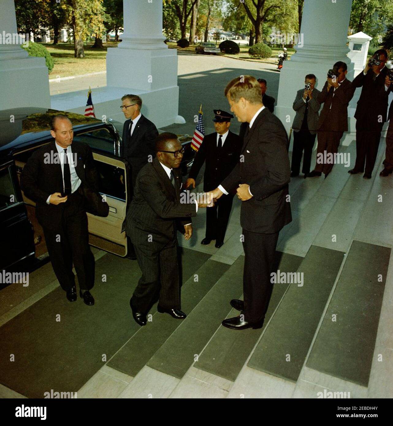 Mittagessen zu Ehren von William Vacanarat Shadrach Tubman, Präsident von Liberia, 1:00 Uhr. Mittagessen zu Ehren von William V.S. Tubman, Präsident von Liberia. (L u2013 R): Protokollchef Angier Biddle Duke; Präsident Tubman; Präsident John F. Kennedy. Verschiedene nicht identifizierte Reporter und Fotografen im Hintergrund. North Portico, White House, Washington, D.C. Stockfoto