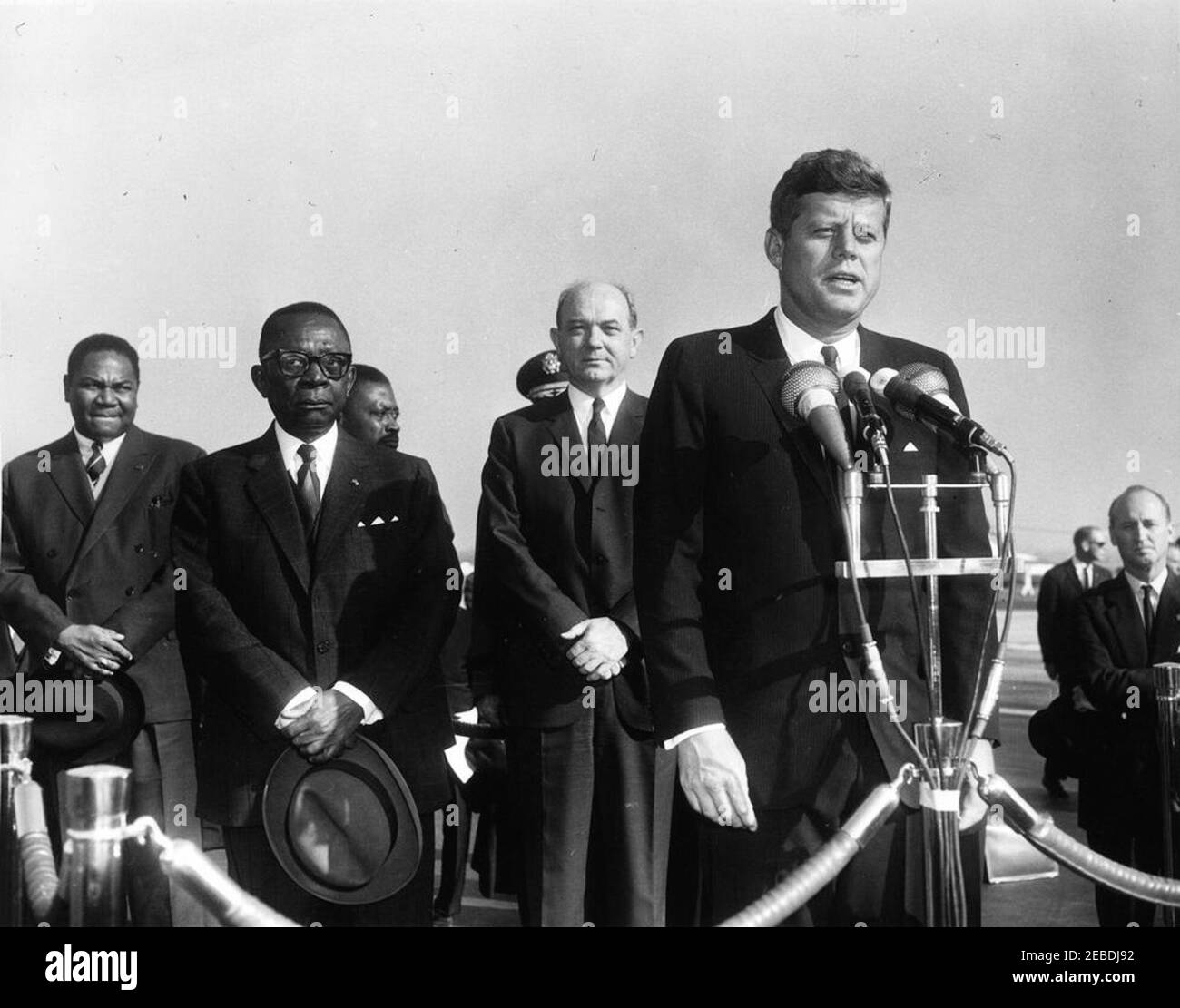 Ankunftszeremonie für William Vacanarat Shadrach Tubman, Präsident von Liberia, 10:00 UHR. Präsident John F. Kennedy hält Bemerkungen bei den Ankunftszeremonien für William V.S. Tubman, Präsident von Liberia. Präsident Kennedy (bei Mikrofonen); Präsident Tubman und Staatssekretär Dean Rusk (hinter Präsident Kennedy); Protokollchef Angier Biddle Duke (rechts von der Plattform); andere nicht identifiziert. Andrews Air Force Base, Maryland. Stockfoto