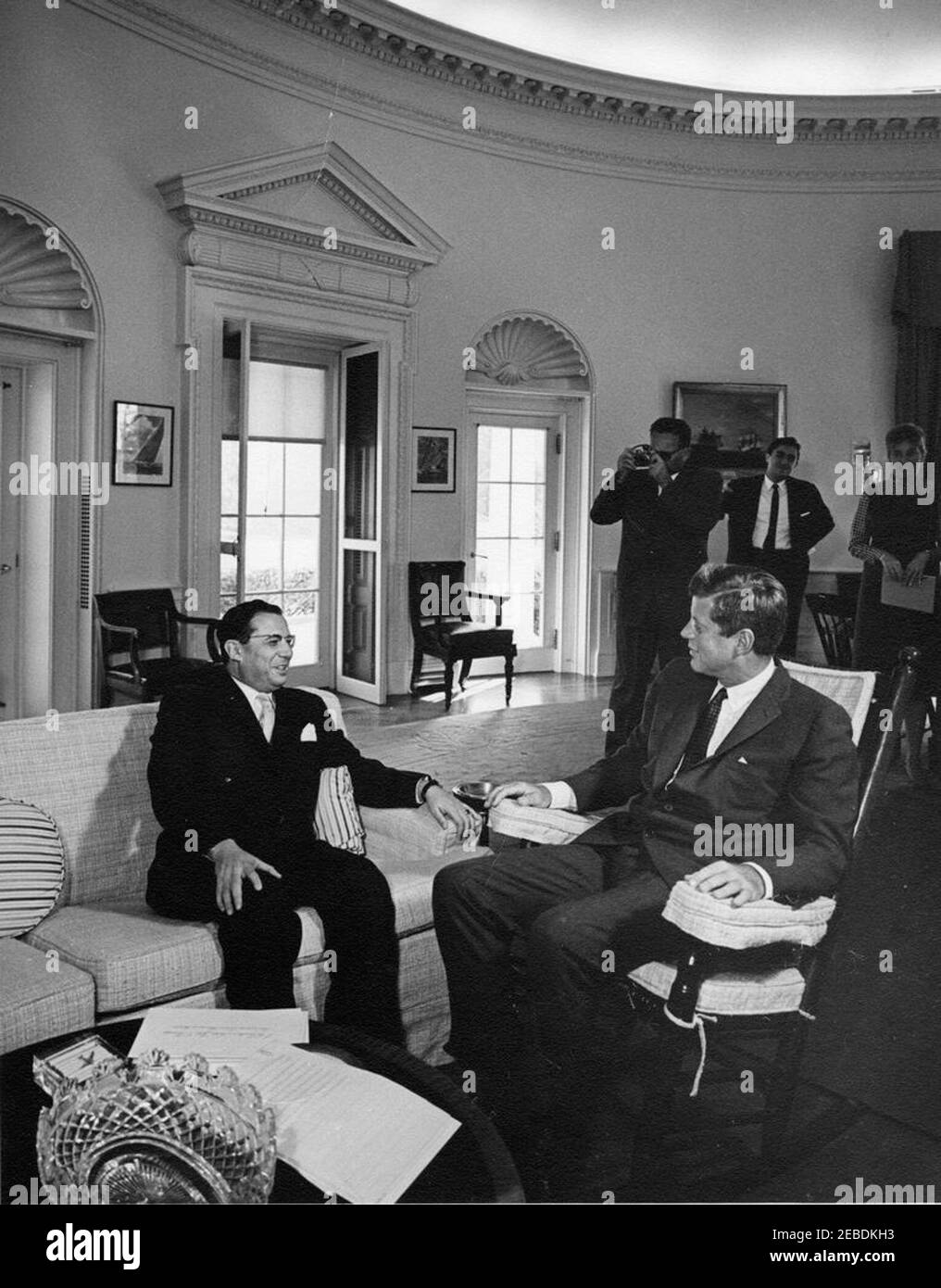 Treffen mit dem Botschafter Brasiliens, Roberto de Oliveira Campos, 11:30am Uhr. Präsident John F. Kennedy (im Schaukelstuhl) trifft sich mit Roberto de Oliveira Campos, Botschafter Brasiliens. Im Hintergrund stehend (L-R): Nicht identifizierter Fotograf; Assistenzspecial Counsel des Präsidenten, Richard u0022Dicku0022 Goodwin; Sekretärin der Assistant Press Secretary, Barbara Gamarekian. Oval Office, White House, Washington, D.C. Stockfoto