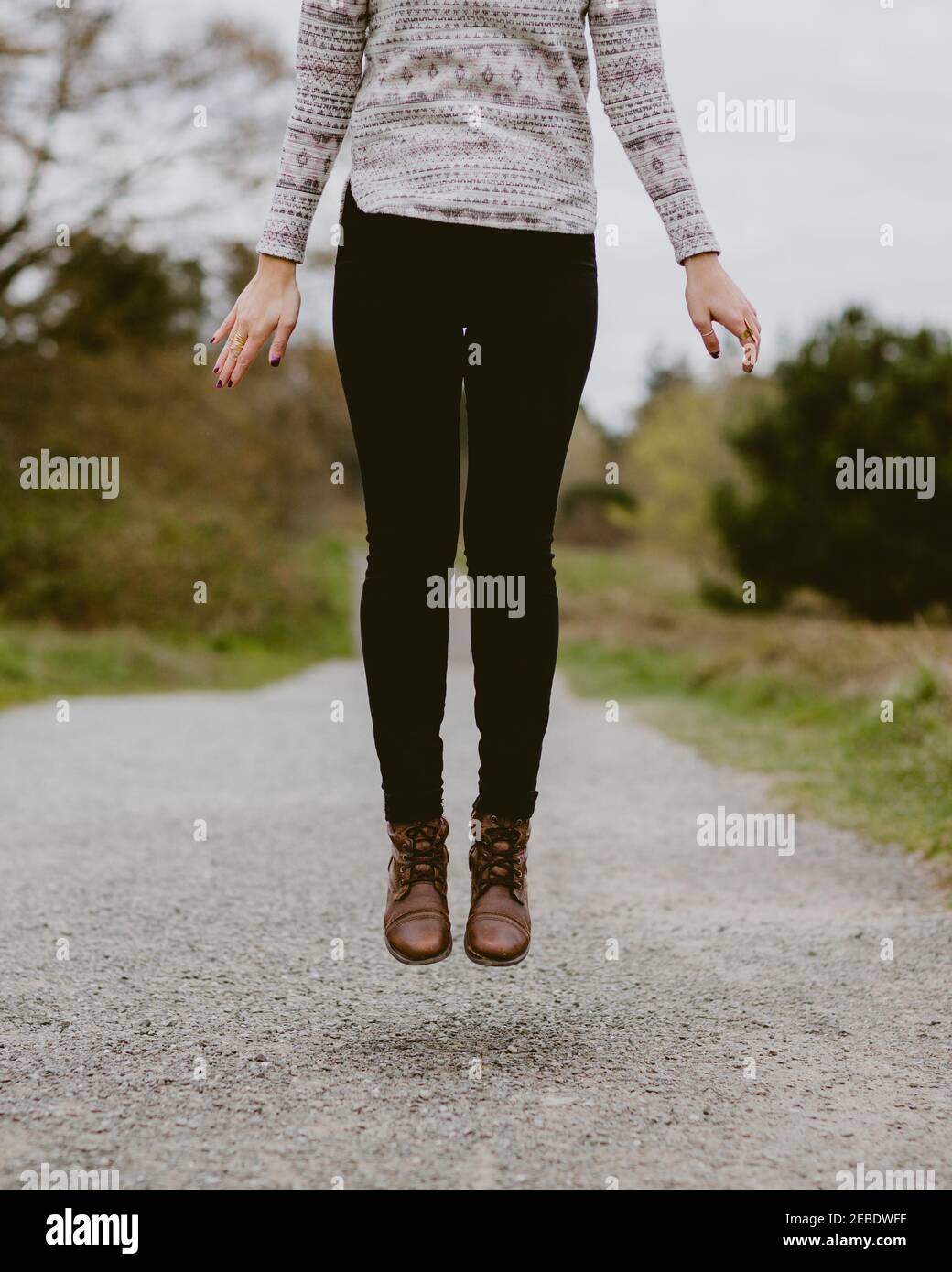 Eine Frau mit Lederstiefeln springt in die Luft Ein Schotterweg Stockfoto
