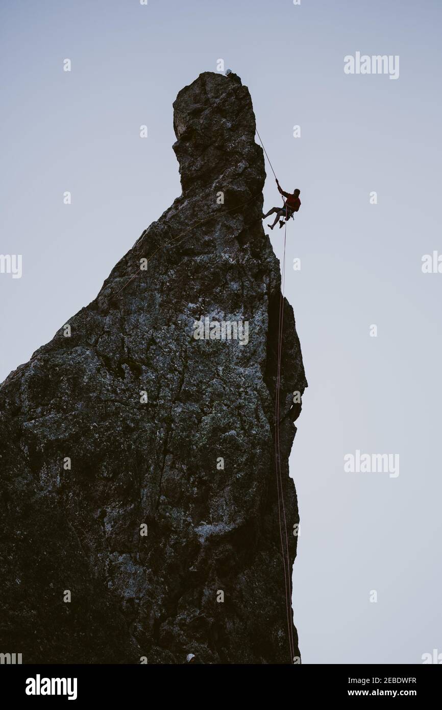 Eine Klettersilhouette rappelt von einem schmalen Gipfel ab Abenddämmerung Stockfoto