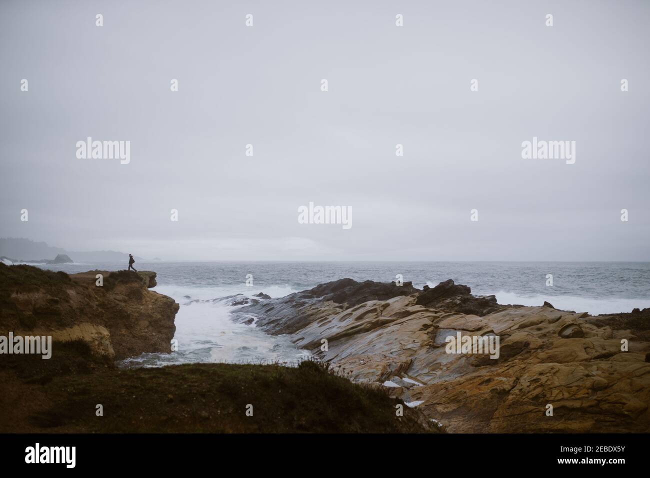 Person geht entlang felsigen Klippen mit Meer und Meer Stapel In der Ferne Stockfoto