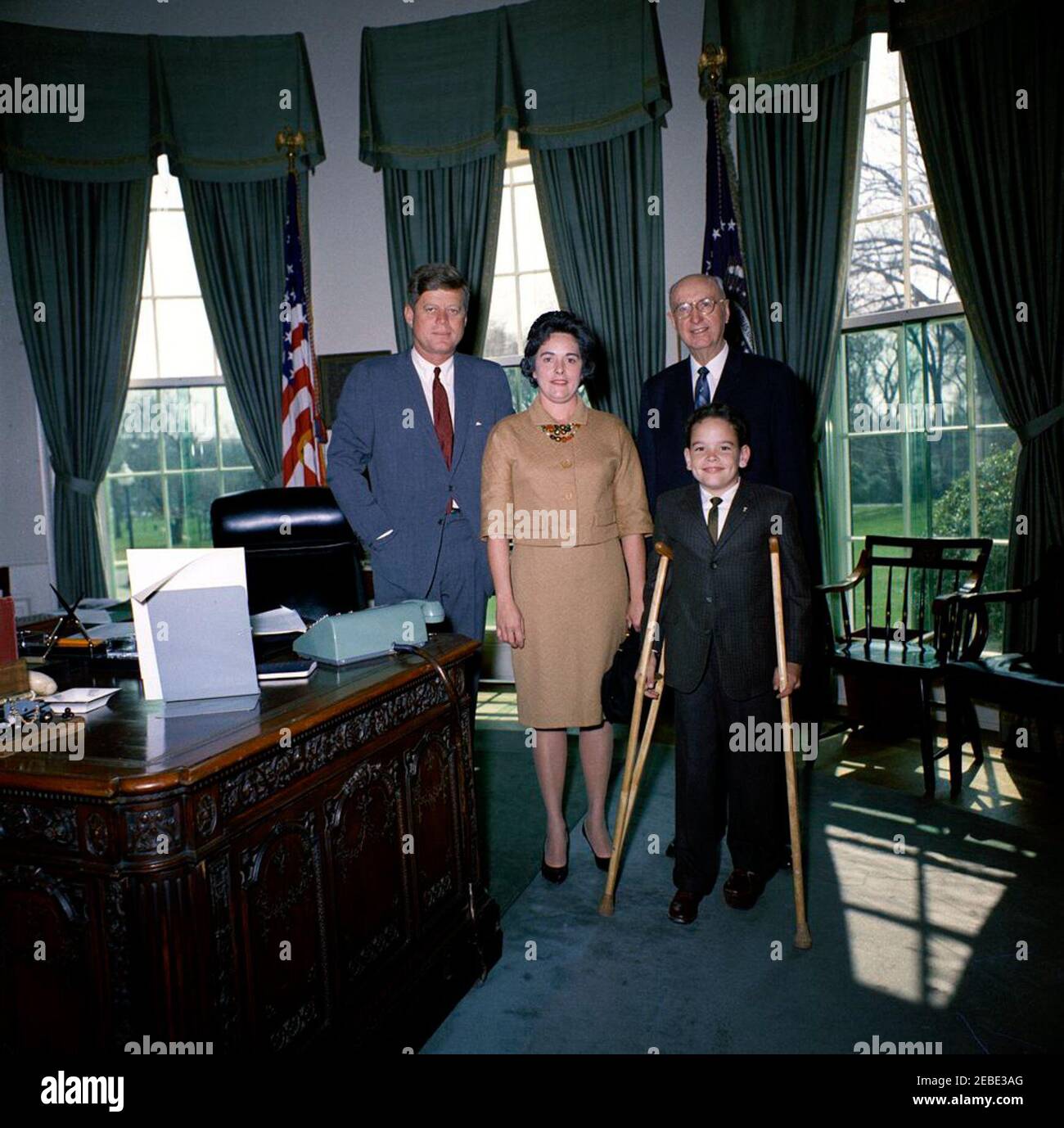 Besuch von Thomas A. Doyle, III, 1962 Ostersiegelkind, 12:07pm. Präsident John F. Kennedy (links) steht mit Thomas A. Doyle, III (rechts vorne), dem 1962 Ostersiegelkind. Zwei weitere Personen sind nicht identifiziert. Ebenfalls im Programm des Präsidenten Kennedyu2019s enthalten: Frau Thomas A. Doyle, Jr.; Präsidentin der National Society of Crippled Children and Adults, Elwood M. Brooks; Direktorin für Öffentlichkeitsarbeit der National Society of Crippled Children and Adults, Catherine Bauer. Oval Office, White House, Washington, D.C. Stockfoto