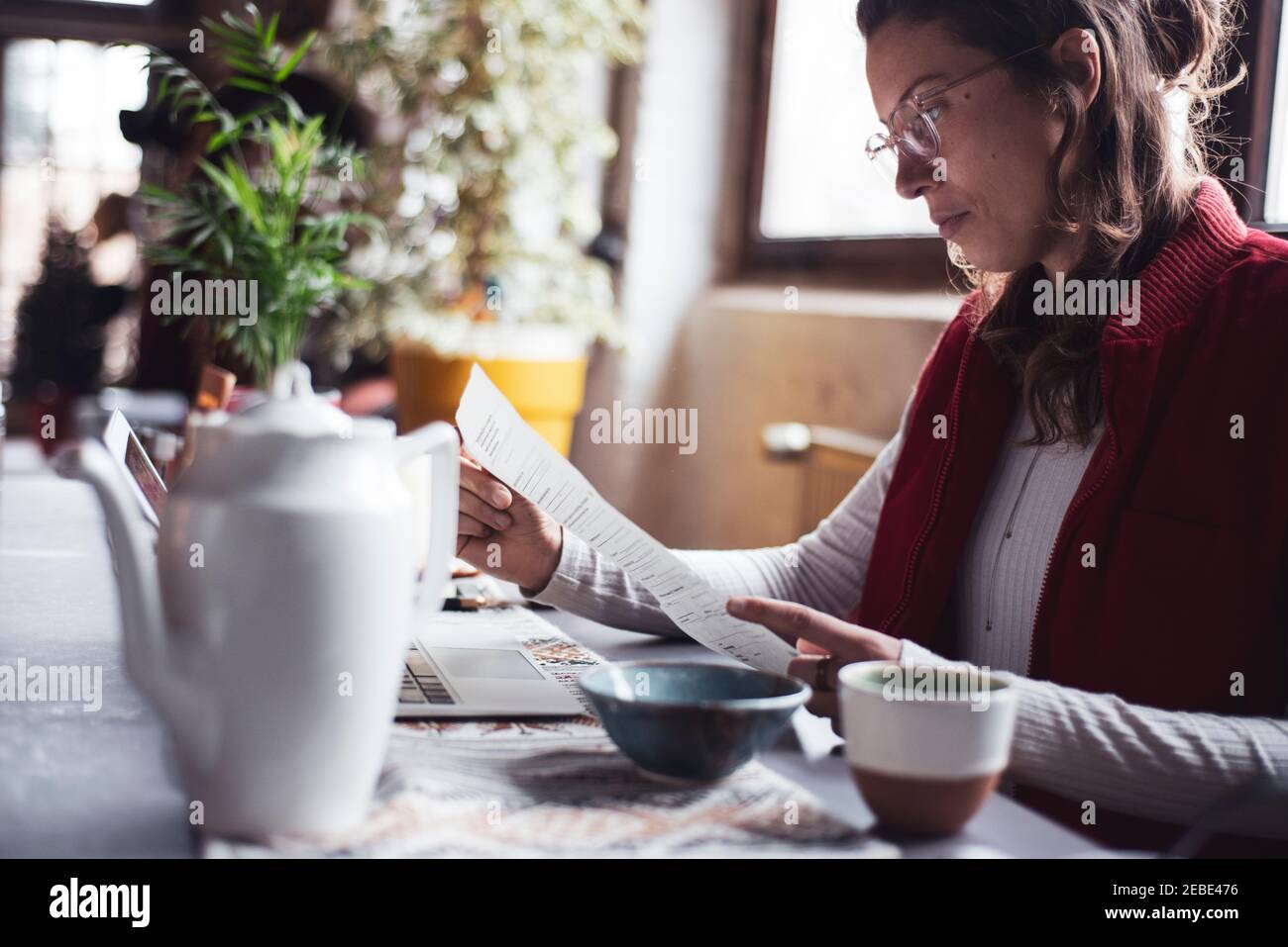 Frau arbeitet von zu Hause aus mit Laptop Papierkram und Tasse Tee Stockfoto