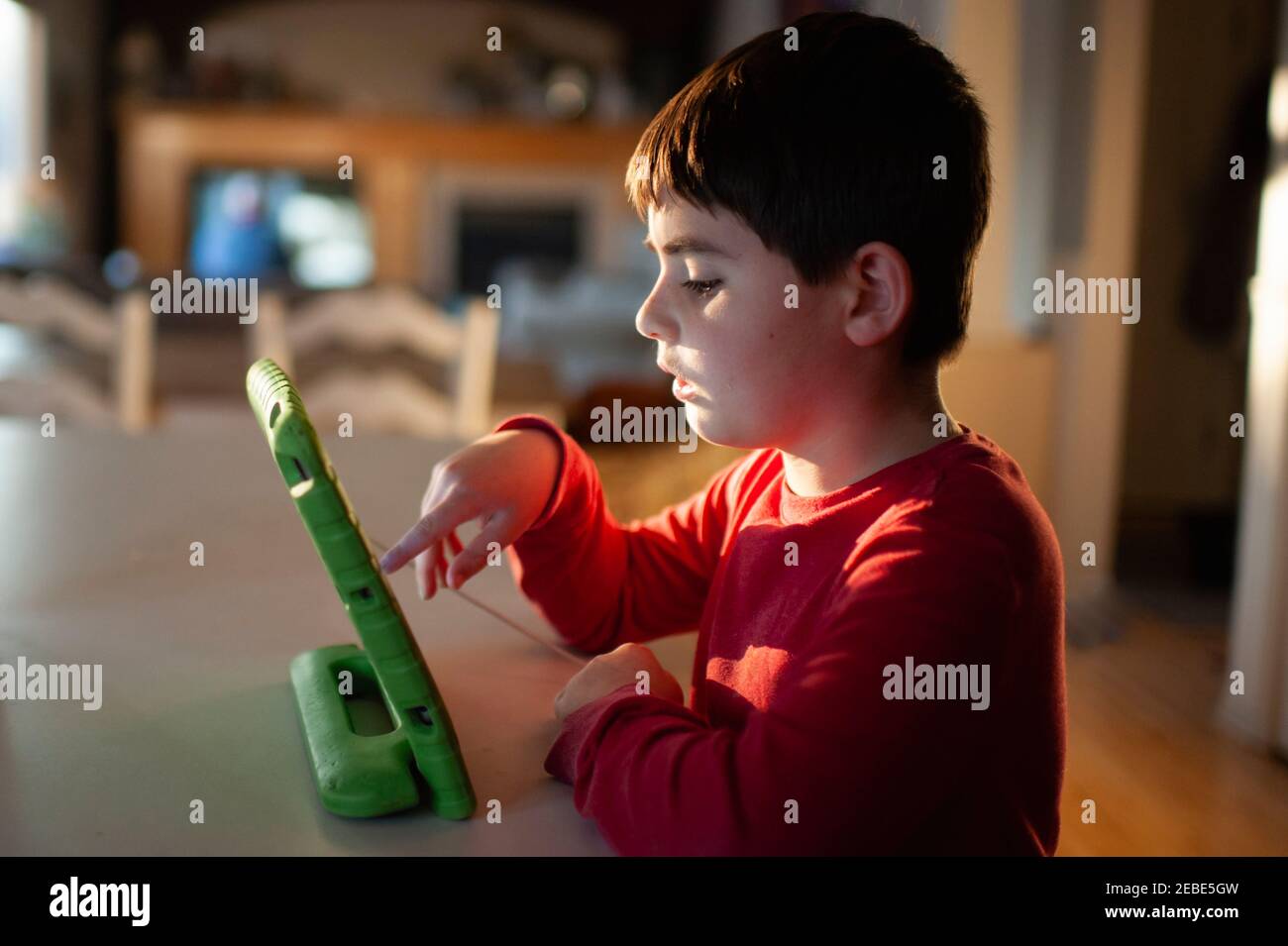 Junge 9-10 Jahre alt spielt mit seinem Tablet an der Küchentisch Stockfoto