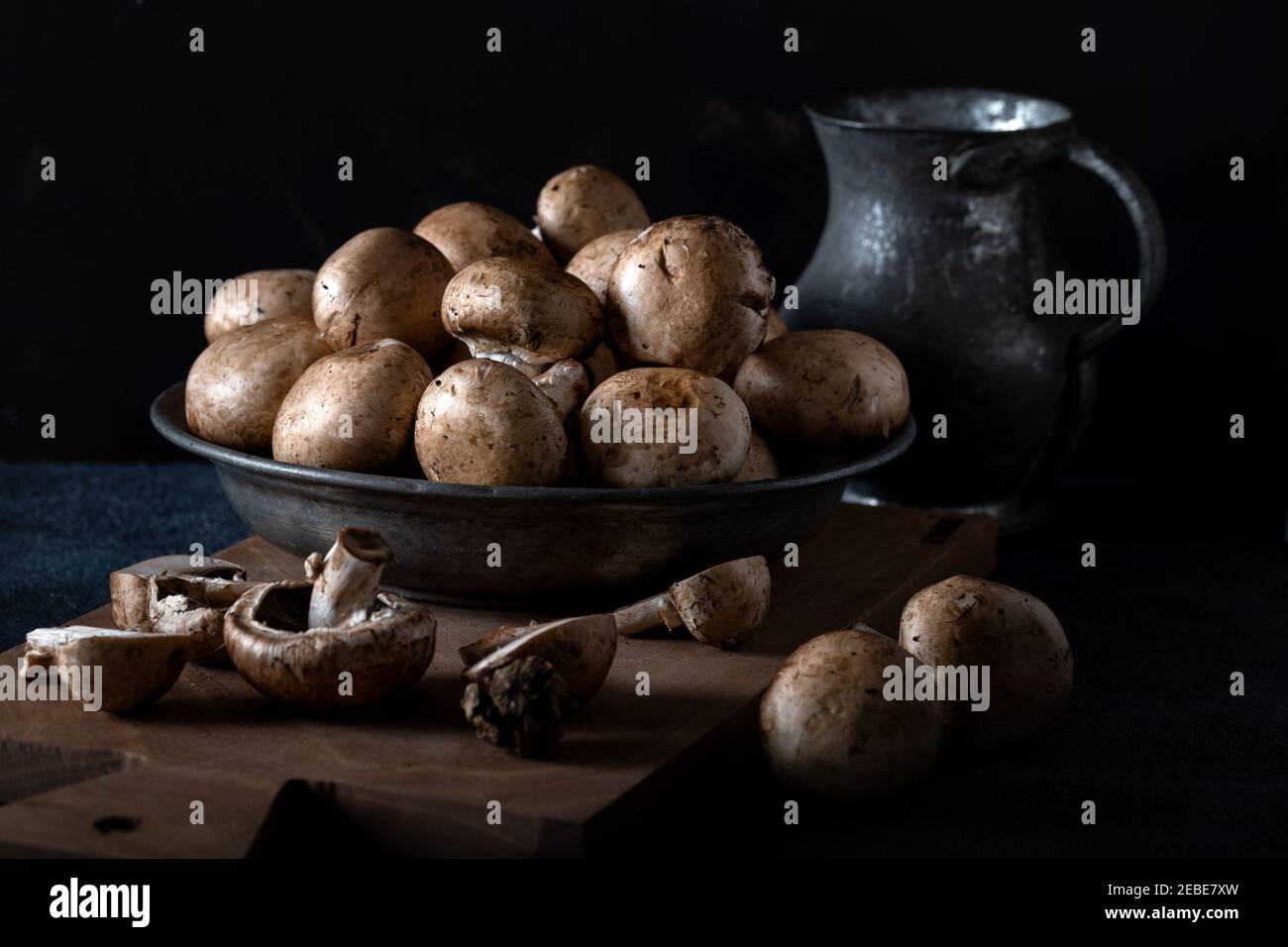 Frische Champignon (Knopf) Pilze in Schüssel auf einem Holzbrett vor dem dunklen Hintergrund. Stockfoto