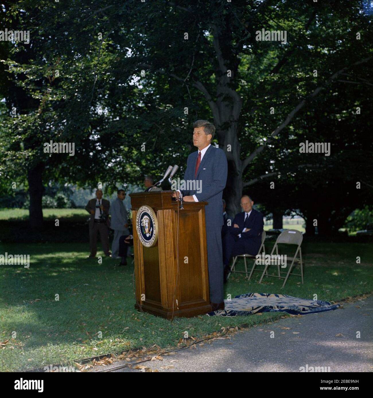 Einführungszeremonie, Workmenu0027s Entschädigung Gedenkmarke, 12:05pm. Präsident John F. Kennedy spricht bei einer Zeremonie anlässlich des 50th. Jahrestages des ersten staatlichen Workmenu0027s-Entschädigungsgesetzes, das 1911 in Wisconsin erlassen wurde, auf der Zufahrt zum South Lawn im Weißen Haus, Washington, D.C., Secretary of the Treasury C. Douglas Dillon sitzt hinter Präsident Kennedy. Stockfoto