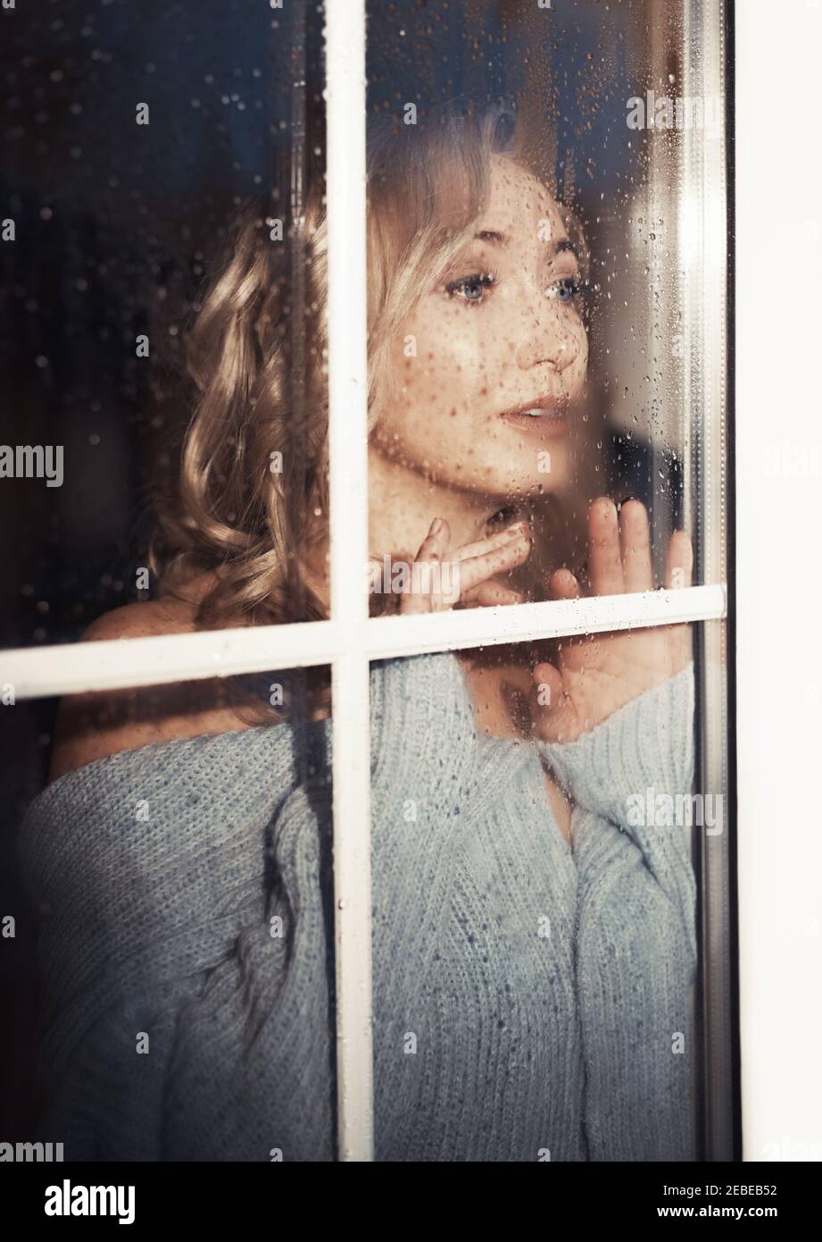Blonde Frau hinter dem nassen Fenster Stockfoto