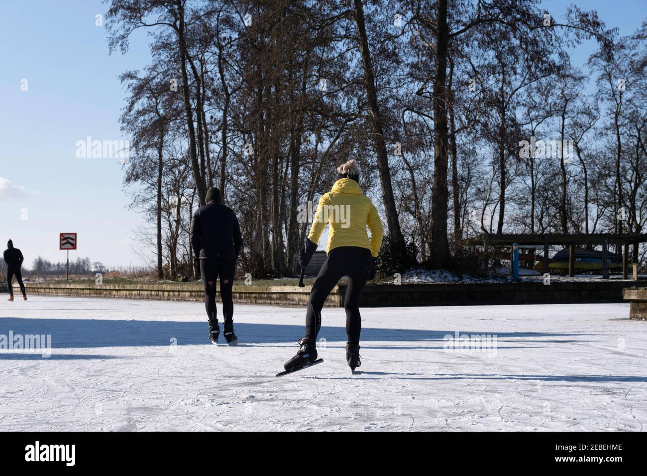 Sportläufer in einer sonnigen und kalten friesischen Landschaft auf einem gefrorenen See in Goingarijp in Friesland. Landschaft mit blau bewölktem Himmel und Bäumen Stockfoto