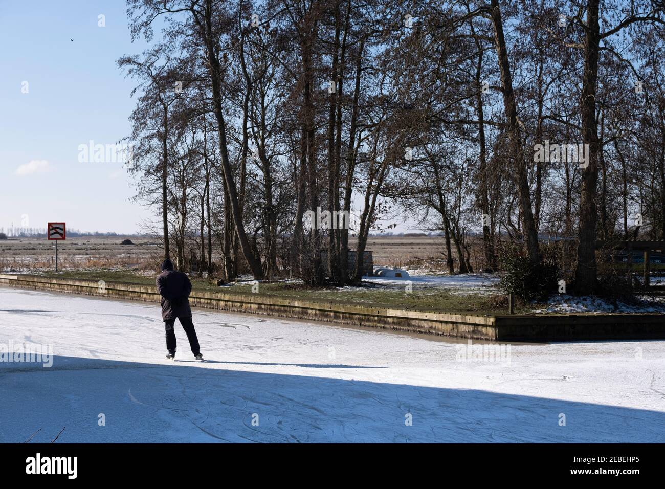 Ältere Freizeitskater in einer sonnigen und kalten friesischen Landschaft auf einem gefrorenen See in Goingarijp in Friesland. Landschaft mit blau bewölktem Himmel und Bäumen Stockfoto