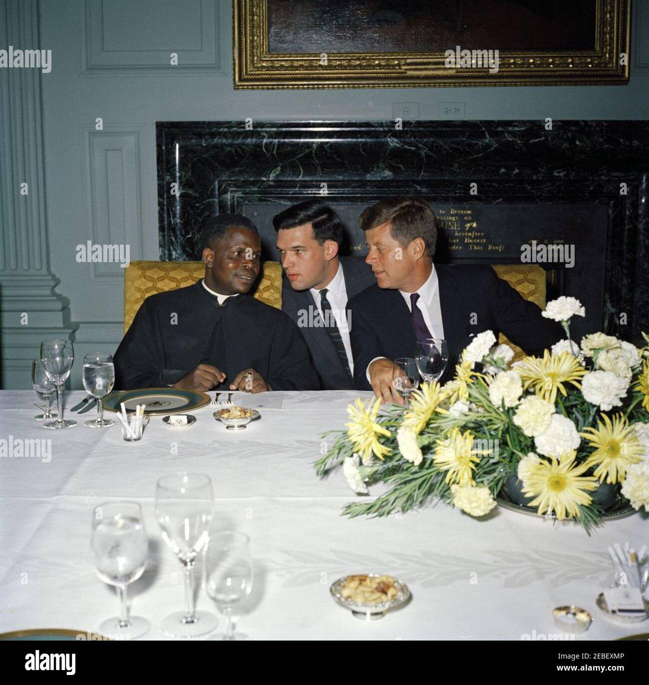 Mittagessen zu Ehren von Fulbert Youlou, Präsident der Republik Kongo (Brazzaville), 1:30pm Uhr. Mittagessen zu Ehren des Präsidenten der Republik Kongo Fulbert Youlou (Brazzaville). (L-R) Präsident Youlou, nicht identifizierter Mann, Präsident John F. Kennedy. Das Gemälde über dem Kamin ist ein 1869 Porträt von Abraham Lincoln von George P.A. Healy und wurde dem Weißen Haus im Jahr 1939 gespendet. Die Inschrift im grünen Marmorkamin wurde von Präsident Franklin D. Roosevelt in Auftrag gegeben und aus einem Brief von John Adams an seine Frau Abigail entnommen, und liest: u201cI Bete Heaven to send the Stockfoto