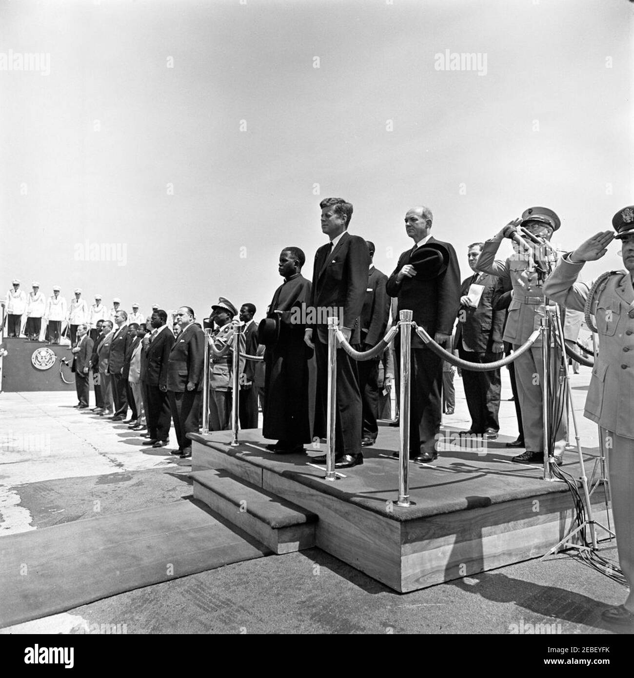 Ankunftszeremonie für Fulbert Youlou, Präsident der Republik Kongo (Brazzaville), 12:00pm Uhr. Ankunftszeremonien für den Präsidenten der Republik Kongo (Brazzaville) Fulbert Youlou. Auf Plattform (L-R): Präsident Youlou, Präsident John F. Kennedy, Botschafter der Republik Kongo (Brazzaville) Emmanuel Damongo Dadet, Staatssekretär Dean Rusk, Dolmetscher des US-Außenministeriums Edmund S. Glenn, Chef des Außenministeriums für Protokoll Angier Biddle Duke (hinter Mikrofonen), Und Kommandant des United States Marine Corps General David M. Shoup. Air Force Aide an den Präsidenten Brig Stockfoto