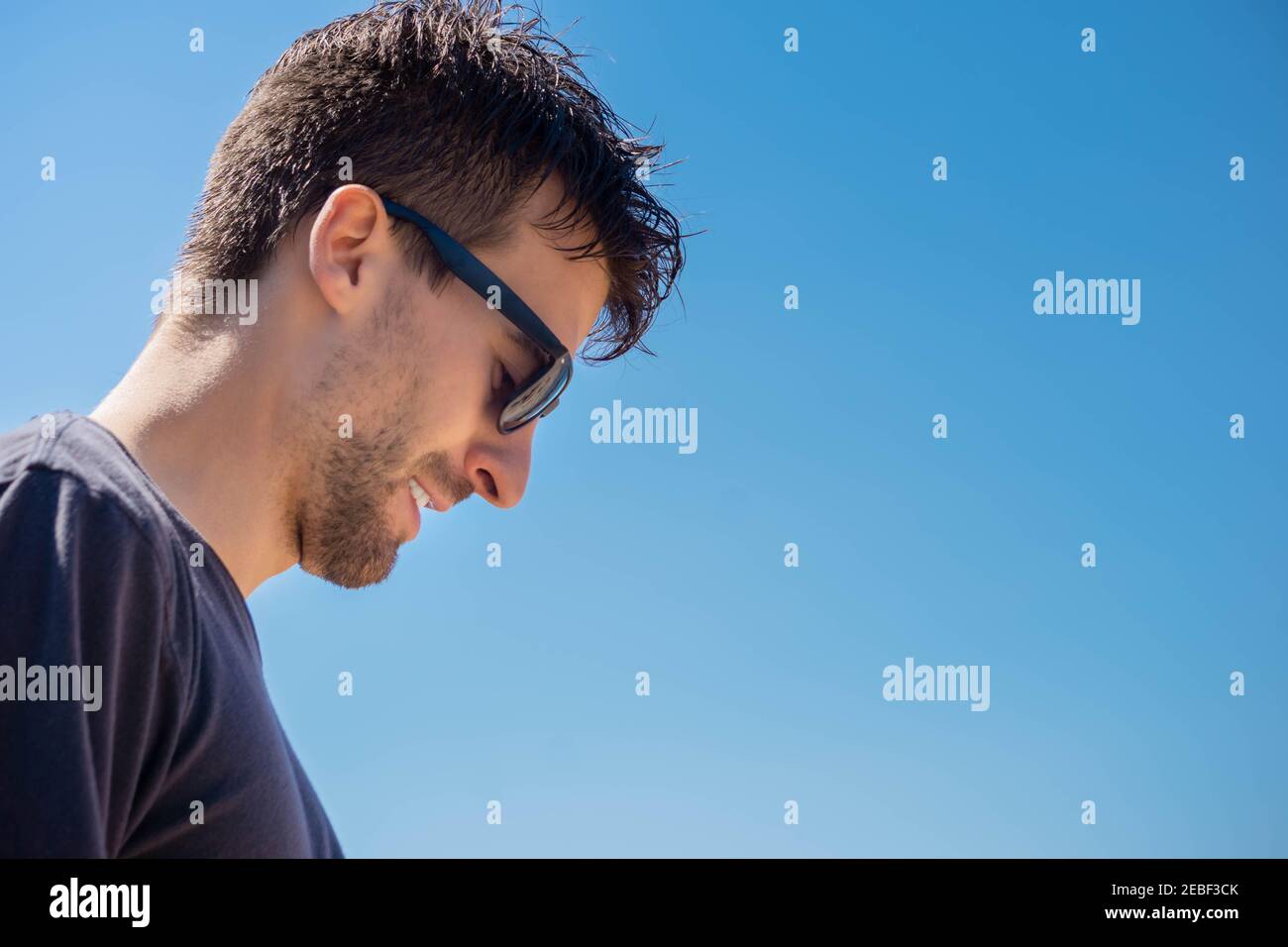 Porträt eines Mannes mit Sonnenbrille neigte seinen Kopf auf Himmel Hintergrund. Schüchterner Kerl im Sonnenbrillen-Portrait. Profil von stilvollen Mann in schwarzem Hemd und Brille Stockfoto
