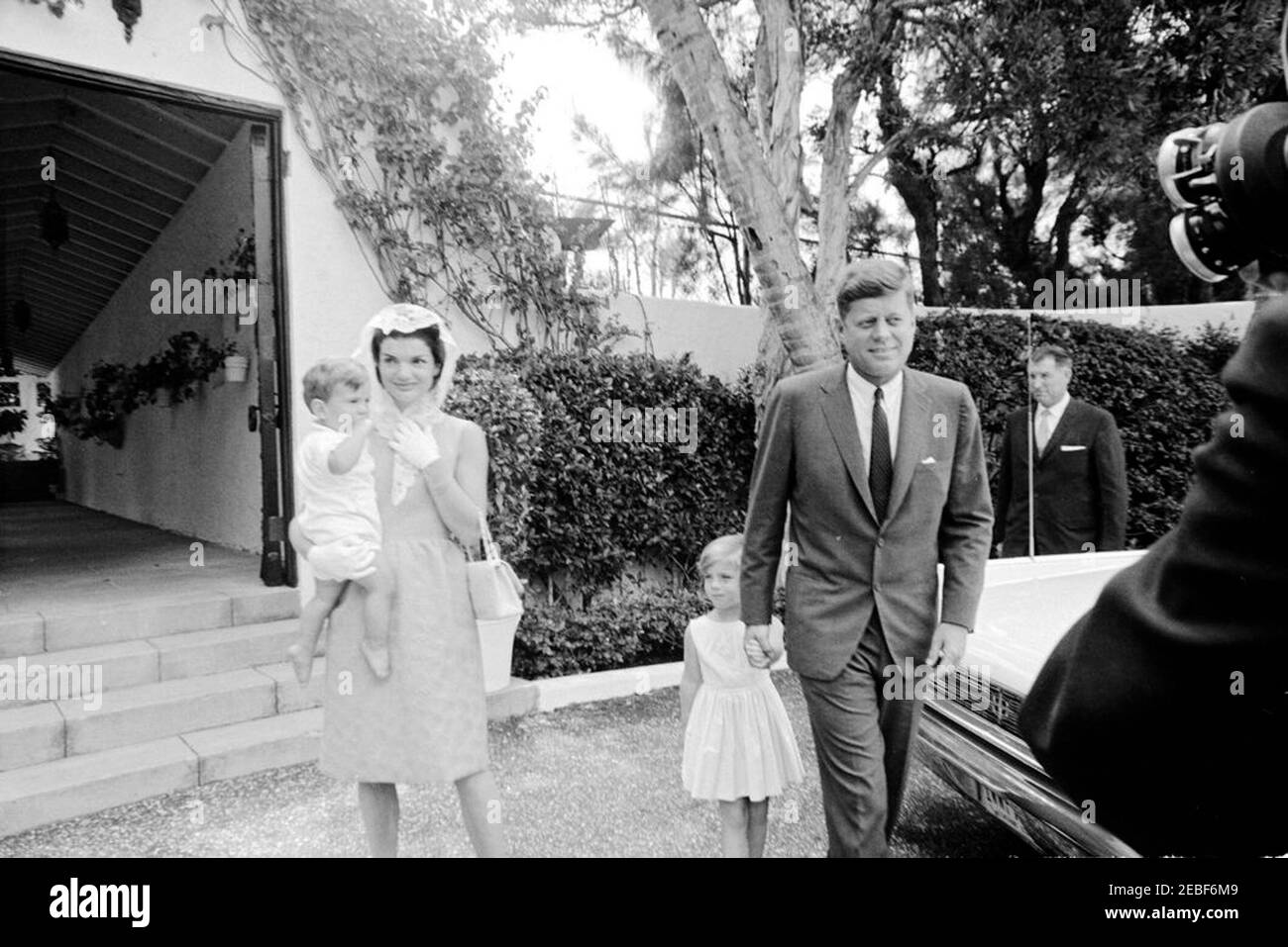 Präsident Kennedy u0026 Familie besuchen Messe in Palm Beach. Die Kennedy-Familie verlässt eine private Kapelle in der Residenz von Botschafter Joseph P. Kennedy, Sr., in Palm Beach, Florida, nach Ostersonntag-Service. Präsident John F. Kennedy hält Caroline Kennedyu0027s Hand; First Lady Jacqueline Kennedy trägt John F. Kennedy, Jr.; White House Secret Service Agent, Bill Greer, steht rechts (hinter dem Auto). Stockfoto