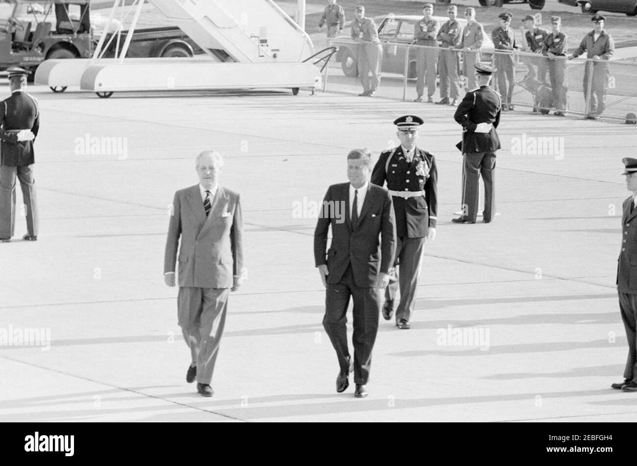 Ankunftszeremonie für Harold Macmillan, Premierminister von Großbritannien, 4:50pm Uhr. Präsident John F. Kennedy geht mit Premierminister von Großbritannien, Harold Macmillan (links), während der Ankunftszeremonien zu Ehren von Premierminister Macmillan. Kommandant der Truppen, Oberstleutnant Charles P. Murray, Jr., geht hinter Präsident Kennedy. Andrews Air Force Base, Maryland. Stockfoto
