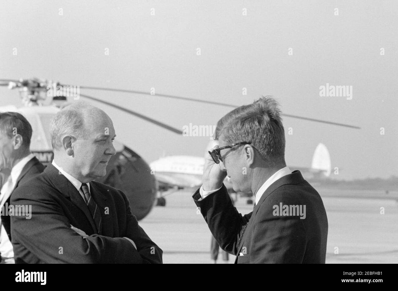 Ankunftszeremonie für Harold Macmillan, Premierminister von Großbritannien, 4:50pm Uhr. Präsident John F. Kennedy (mit Sonnenbrille) steht mit Staatssekretär Dean Rusk bei den Ankunftszeremonien zu Ehren des britischen Premierministers Harold Macmillan. Minister in der britischen Botschaft, Lord Hood (Viscount Samuel Hood), steht im Hintergrund ganz links, meist versteckt am Rand des Rahmens. Andrews Air Force Base, Maryland. Stockfoto