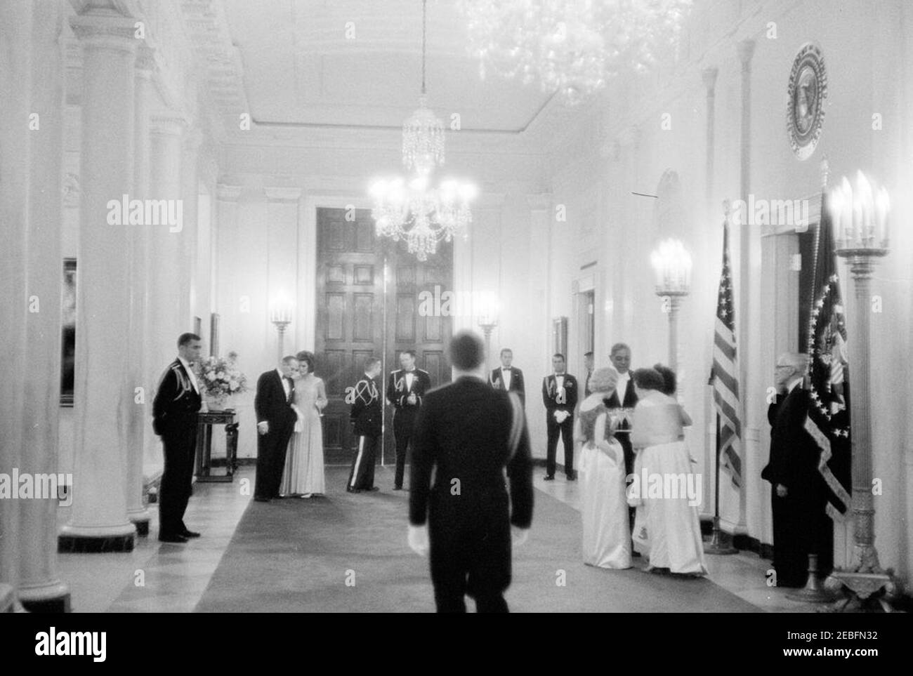 Abendessen zu Ehren der Nobelpreisträger, 8:00pm Uhr. First Lady Jacqueline Kennedy spricht mit dem Schauspieler Frederic March (beide im Hintergrund links) bei einem Abendessen zu Ehren der Nobelpreisträger aus der westlichen Hemisphäre; Mr. March führte zu diesem Anlass eine Lesung durch. Militärische Seite des Präsidenten, General Chester V. Clifton, steht rechts von Frau Kennedy. Cross Hall, White House, Washington, D.C. Stockfoto