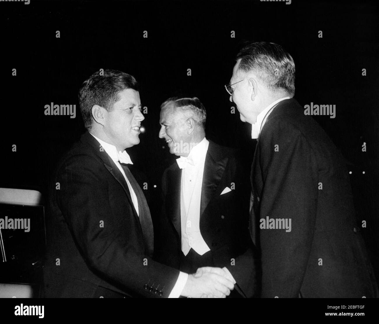 Gridiron Club Abendessen, 6:54pm Uhr. Gridiron Club Abendessen. Präsident John F. Kennedy schüttelte sich die Hände mit dem Präsidenten des Gridiron Clubs, Robert L. Riggs; General Manager des Statler Hilton Hotels, Herbert Blunck (in der Mitte stehend). Außerhalb des Statler Hilton Hotels, Washington, D.C., rnrn Stockfoto