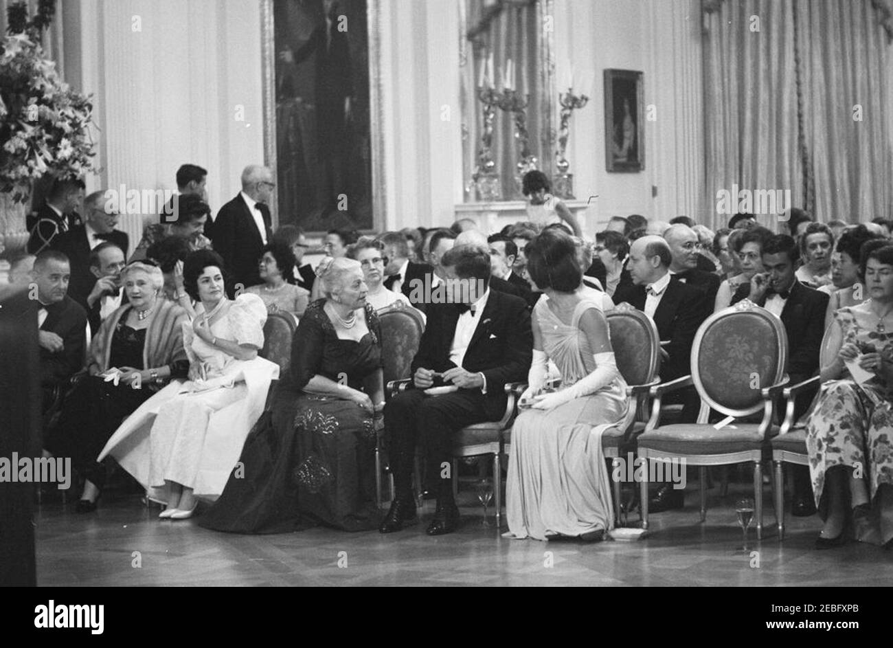 Abendessen zu Ehren der Nobelpreisträger, 8:00pm Uhr. Präsident John F. Kennedy und andere treffen sich im East Room, um bei einer Lesung des Schauspielers Frederic March von Auszügen aus den Werken der späten amerikanischen Nobelpreisträger während eines Abendessens zu Ehren der Nobelpreisträger aus der westlichen Hemisphäre teilzunehmen. Präsident Kennedy und First Lady Jacqueline Kennedy besuchen mit der Nobelpreisträgerin Pearl S. Buck. Platz in der ersten Reihe (L-R): Vizepräsident Lyndon B. Johnson (meist versteckt); Katherine Tupper Marshall (Witwe des Nobelpreisträgers und ehemaligen Staatssekretärs, General George C. Marshall); Lady Bird Stockfoto