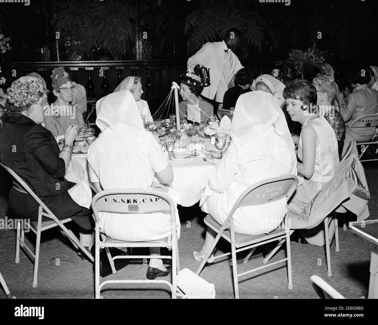 First Lady Jacqueline Kennedy (JBK) nimmt am Mittagessen der Rotkreuzeinheit des Senats Ladiesu0027 Teil. First Lady Jacqueline Kennedy (rechts, im Hintergrund) und Mitglieder der Senate Ladies Red Cross Unit nehmen an einem Mittagessen in der Old Supreme Court Chamber, United States Capitol Building, Washington, D.C. Teil.das Rote Kreuz (auch bekannt als u201cLadies der Senateu201d) Besteht aus den Ehefrauen von Mitgliedern des US-Senats. Jean Duff, Ehefrau des ehemaligen Senators James H. Duff (Pennsylvania), sitzt ganz links; Phyllis Ellsworth Dillon, Ehefrau von Secretary of the Treasury, C. Douglas Dillon, sitzt ganz rechts Stockfoto