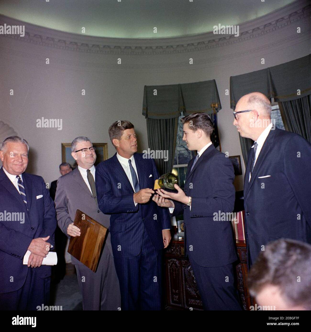 Besuch des Boysu0027 Clubsu0027 u0022Boy des Jahres,u0022 Stephen Lutz, 10:57AM. Präsident John F. Kennedy (Mitte) hält ein Modell im Maßstab, eingeschlossen in einer Flasche, von PT Boot 109, präsentiert ihm von den Boysu0027 Clubs von Americau0027s (BCA) u0022Boy der Yearu0022 Stephen Lutz von Newark, New Jersey. (L-R) Albert L. Cole, Präsident der BCA; nicht identifizierter Mann (hinten, teilweise versteckt); John M. Gleason, Nationaldirektor der BCA; Präsident Kennedy; Stephen Lutz; und Charles R. Messier, Executive Director der Boysu0027 Clubs von Newark, New Jersey. Ovales Büro, Weißes Haus, Stockfoto