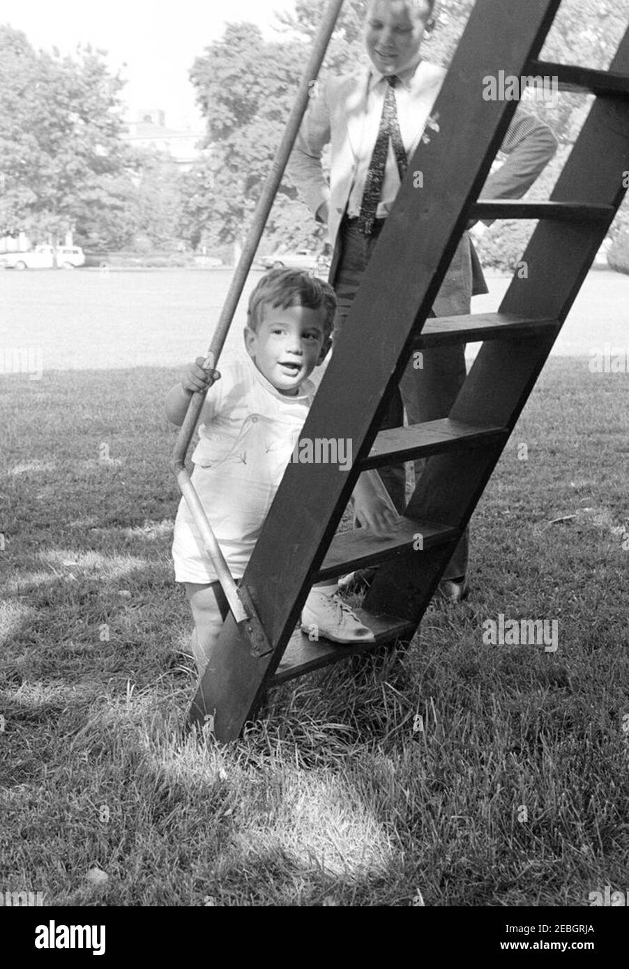 Vizepräsident Lyndon B. Johnson (LBJ) präsentiert Caroline Kennedy (CBK) ein neues Pony, u201cTexu201d; Kinder spielen auf dem South Lawn. John F. Kennedy, Jr., klettert die Leiter eines Baumhauses auf dem South Lawn des Weißen Hauses; ein nicht identifizierter Junge steht hinter ihm. Washington, D.C. Stockfoto