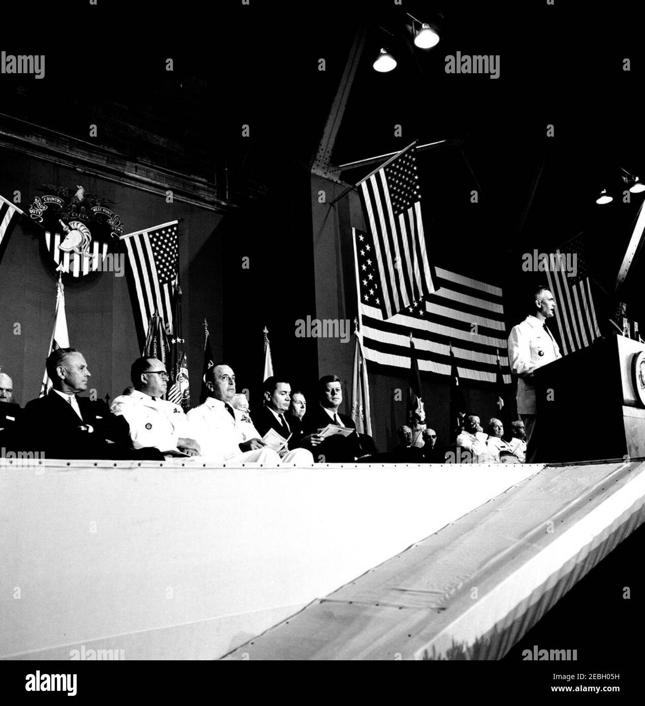 Festrede an der United States Military Academy, West Point (New York), 10:01AM Uhr. Der Superintendent der United States Military Academy (USMA), Generalmajor William C. Westmoreland (rechts, am Rednerpult), hält Bemerkungen während der Abschlussübungen an der USMA, West Point, New York. Ebenfalls abgebildet (auf der Bühne sitzend): General Maxwell D. Taylor; Stabschef der United States Army, General George H. Decker; Chairman of the Joint Chiefs of Staff, General Lyman L. Lemnitzer; Sekretär der Armee, Elvis J. Stahr, Jr.; Präsident John F. Kennedy; Militärische Aide an den Präsidenten, General Cheste Stockfoto