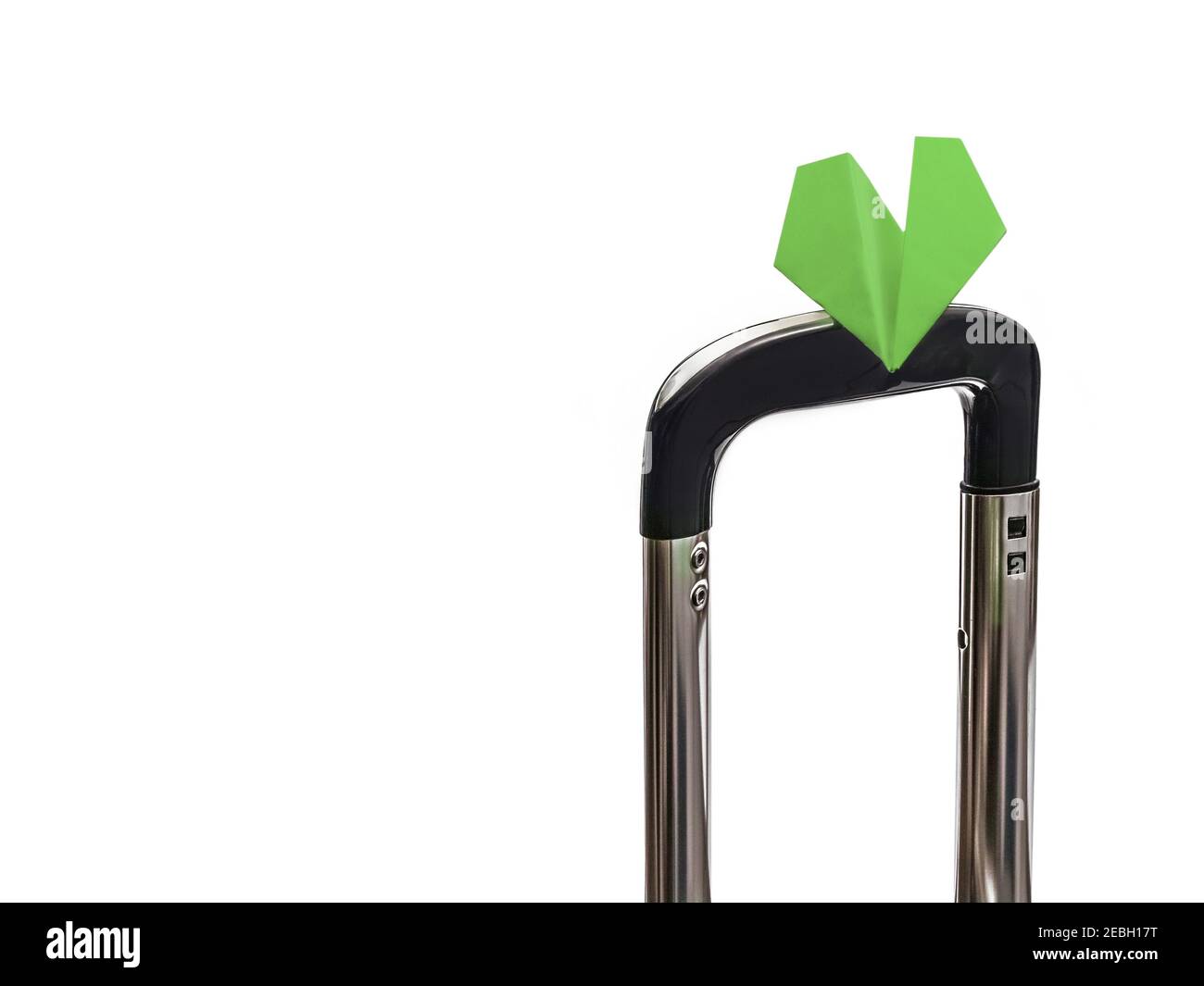 Auf dem ausdehnbaren Griff des Handgepäcks ruht ein kleines Papierflugzeug wie ein grüner Schmetterling. Stockfoto