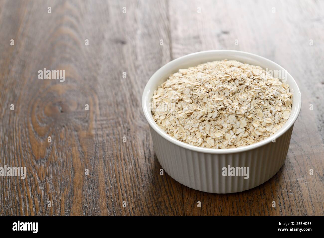 Keramikschale mit gerolltem Hafer auf dunklem Hickory-Holz Planken Stockfoto