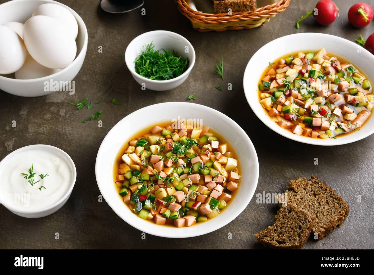 Kalte russische Suppe Okroshka mit Wurst, Gemüse und Kvass auf braunem Hintergrund. Leckeres Sommergericht zum Abendessen. Stockfoto