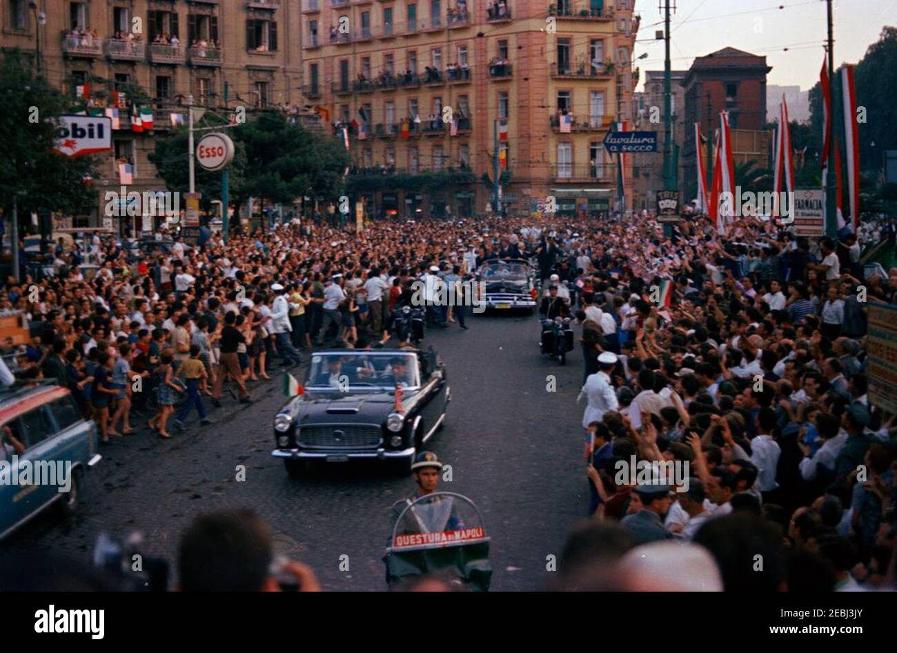 Europareise: Italien, Neapel: Autokolonne, 5:40pm Uhr. Präsident John F. Kennedy (im zweiten Auto stehend) winkt aus einem offenen Cabrio, während seine Autokolonne durch Neapel, Italien, fährt. Präsident von Italien, Antonio Segni, steht mit Präsident Kennedy. Ebenfalls im Bild: Special Assistant to President Kennedy, Kenneth P. Ou2019Donnell; White House Secret Service Agents, Dave Grant, Floyd Boring, James J. Rowley und Roy Kellerman. Eine Motorradbegleitung fährt mit der Autokolonne; Menschenmassen säumen die Straße. Stockfoto