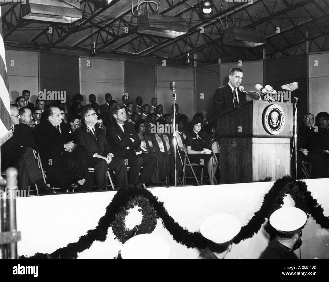 Beleuchtungszeremonie, nationaler Weihnachtsbaum an der Ellipse, 5:15pm Uhr. Innenminister Stewart L. Udall (am Rednerpult) hält Bemerkungen bei der Beleuchtung des National Christmas Tree während des National Capital Christmas Pageant of Peace in der Ellipse, Presidentu2019s Park, Washington, D.C., sitzt links von Rednerpult in der ersten Reihe (R-L): Präsident John F. Kennedy; Unterstaatssekretär James K. Carr; Botschafter Nicaraguas und Dekan des Diplomatischen Korps, Dr. Guillermo Sevilla-Sacasa; nicht identifiziert. Im Hintergrund sitzen Mitglieder des Tuskegee Institute Choir. [Blatt Papier adher Stockfoto