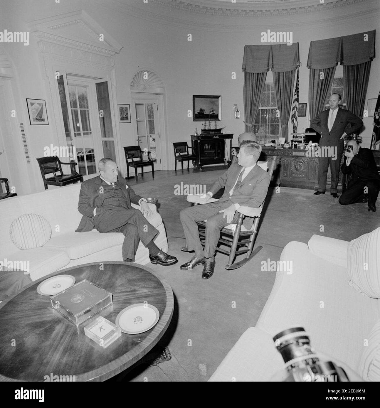 Treffen mit Botschafter von Japan, Koichiro Asakai, 4:00pm Uhr. Präsident John F. Kennedy (im Schaukelstuhl) trifft sich mit dem japanischen Botschafter Koichiro Asakai; der Botschafter stattete Präsident Kennedy einen Abschiedsbesuch ab, bevor er seinen Posten ablegte. Rechts im Hintergrund: Chef des Protokolls, Angier Biddle Duke; New York Times Fotograf, George Tames. Oval Office, White House, Washington, D.C. Stockfoto