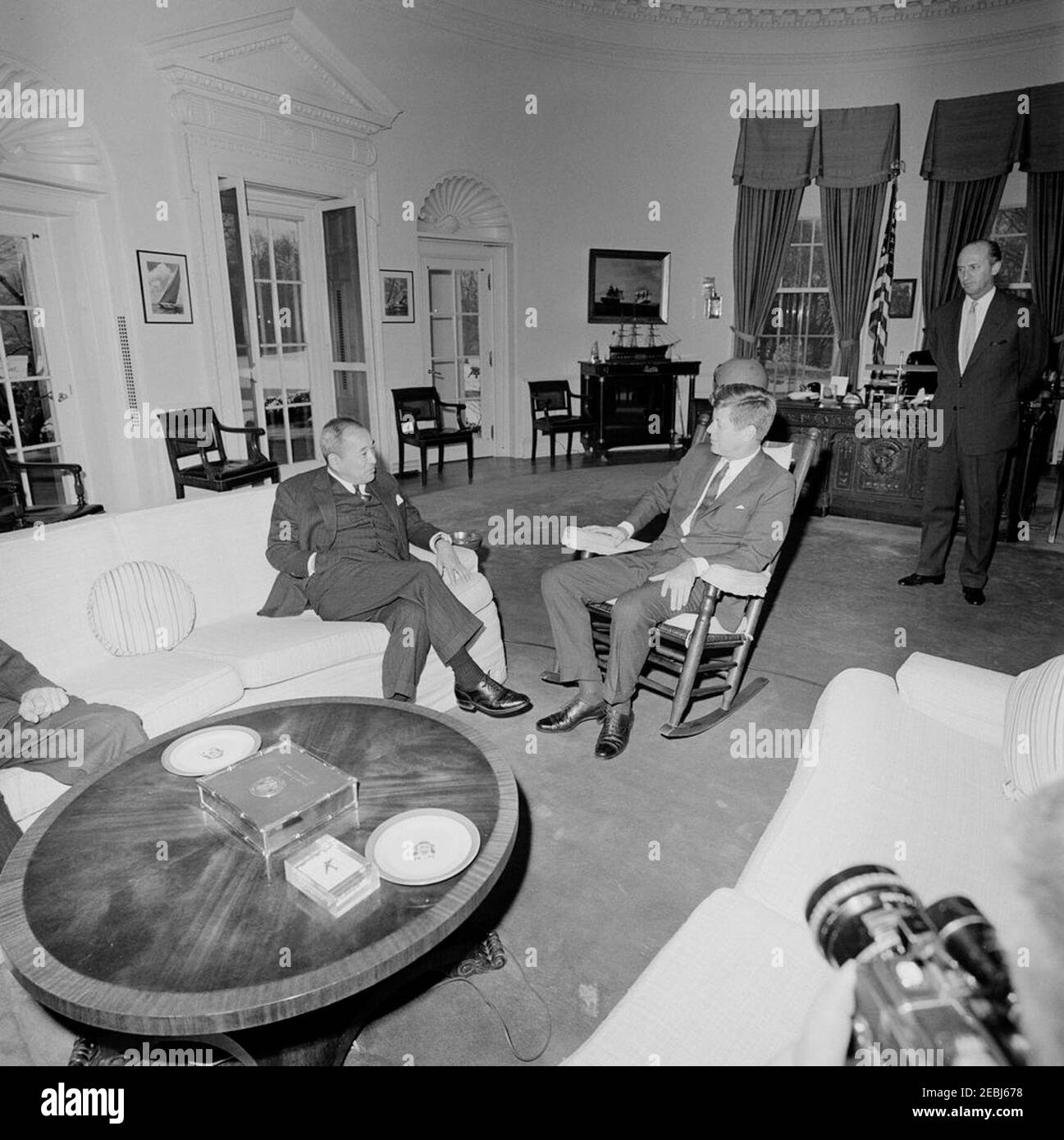 Treffen mit Botschafter von Japan, Koichiro Asakai, 4:00pm Uhr. Präsident John F. Kennedy (im Schaukelstuhl) trifft sich mit dem japanischen Botschafter Koichiro Asakai; der Botschafter stattete Präsident Kennedy einen Abschiedsbesuch ab, bevor er seinen Posten ablegte. Chef des Protokolls, Angier Biddle Duke, steht rechts im Hintergrund. Oval Office, White House, Washington, D.C. Stockfoto