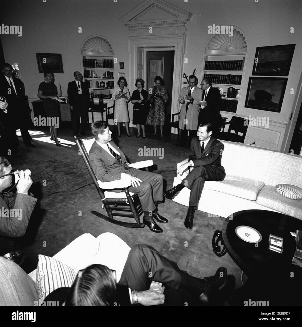 Treffen mit Carl Sanders, gewählter Gouverneur von Georgien, 11:45am Uhr. Präsident John F. Kennedy (in Schaukelstuhl) trifft Gouverneur-elect von Georgien, Carl Sanders. Im Hintergrund stehen: Sekretärin der stellvertretenden Pressesekretärin, Barbara Gamarekian; Sonderassistent des Präsidenten, Dave Powers; Korrespondentin des Weißen Hauses für United Press International (UPI), Helen Thomas. Oval Office, White House, Washington, D.C. Stockfoto