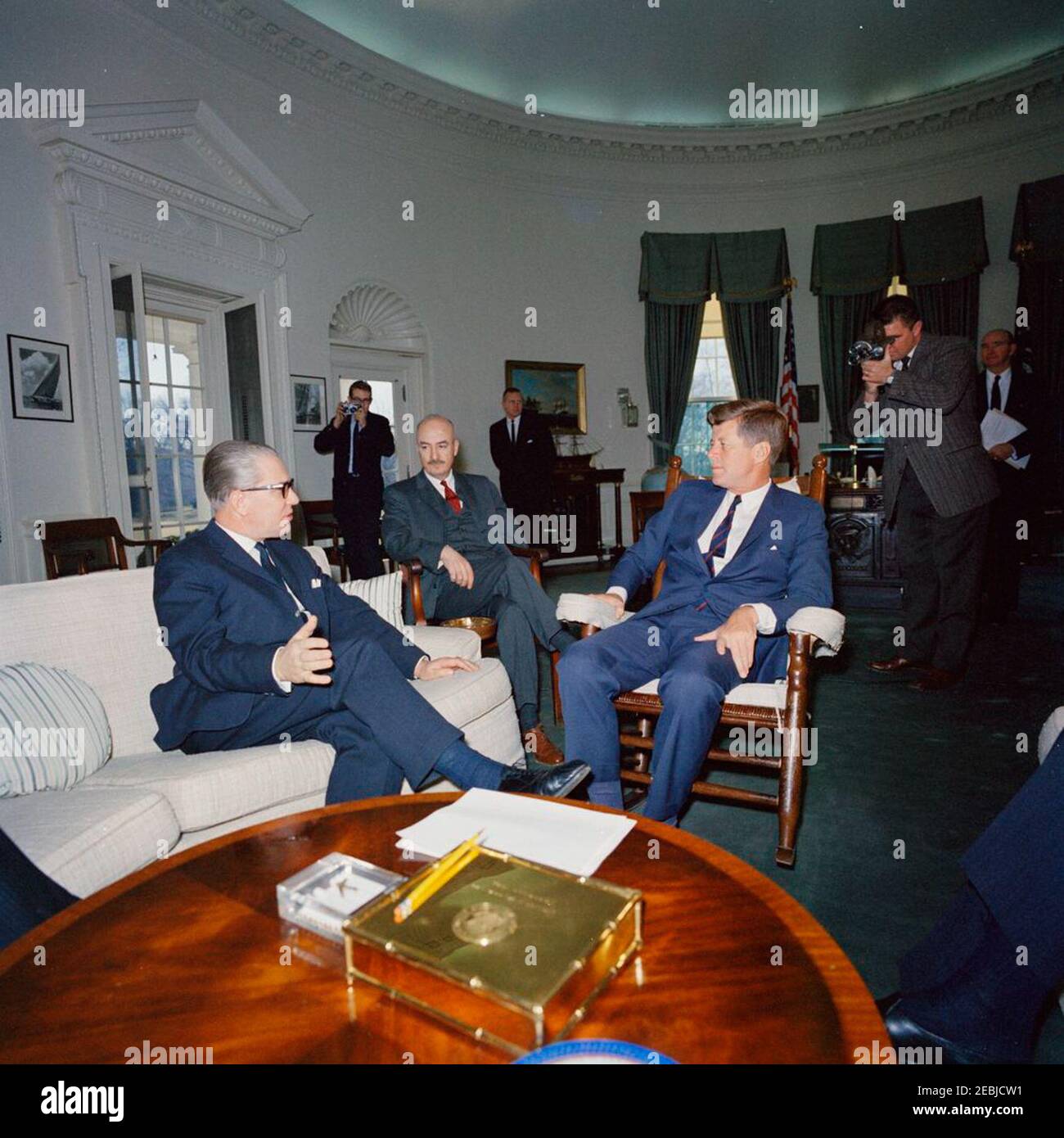 Treffen mit Kai-Uwe von Hassel, Verteidigungsminister der Bundesrepublik Deutschland, 10:00am Uhr. Präsident John F. Kennedy (im Schaukelstuhl) trifft Bundesverteidigungsminister Kai-Uwe von Hassel. Der US-Staatssekretär für europäische Angelegenheiten, William Tyler, sitzt zwischen Präsident Kennedy und Minister von Hassel. Im Hintergrund stehend (L-R): Nicht identifizierter Fotograf; White House Secret Service Agent, Frank Yeager; Filmfotograf für Columbia Broadcasting System (CBS), Tom J. Craven, Jr.; Special Assistant to the President, Dave Powers. Oval Office, White House, Washi Stockfoto