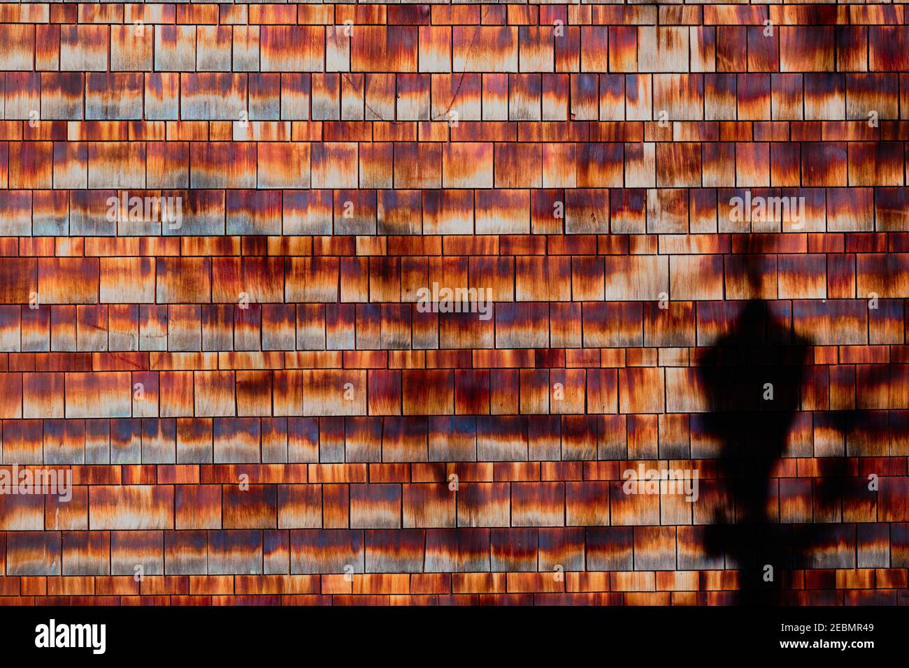 Gepflegte Reihen aus Zedernschindel - feucht und verwittert - zeigen eine Reihe von analogen Farben von orange bis kastanienbraun. Straßenlicht wirft Schatten auf eine Ecke. Stockfoto