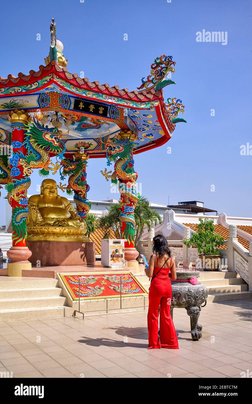 Goldener Buddha-Schrein. Eine Frau in Rot, die einer verzierten chinesischen Pagode, in der ein lachender goldener Buddha untergebracht ist, Respekt zollt. Na Klua Tempel, Pattaya Thailand Stockfoto