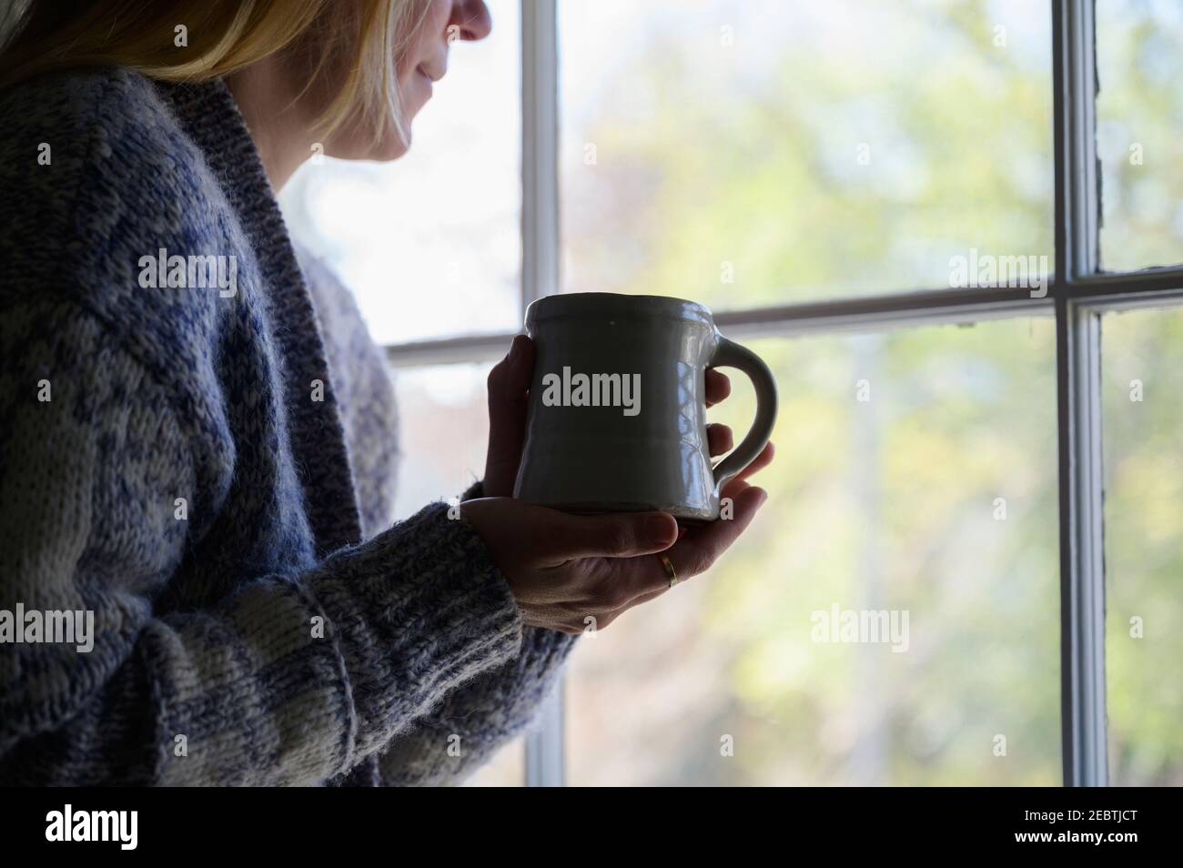 Frau hält Becher und schaut aus dem Fenster Stockfoto