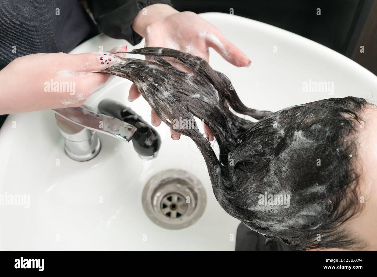 Friseurin waschen lange Haare der Brünette Frau mit Shampoo in Spezielles Waschbecken für die Haarwäsche im Schönheitssalon Stockfoto