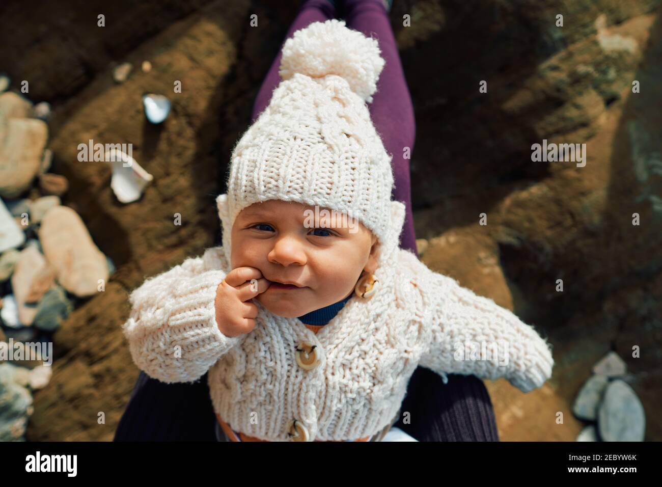 Ein kleines Baby ruht auf dem Schoß der Mutter auf einem Strand im Winter Stockfoto