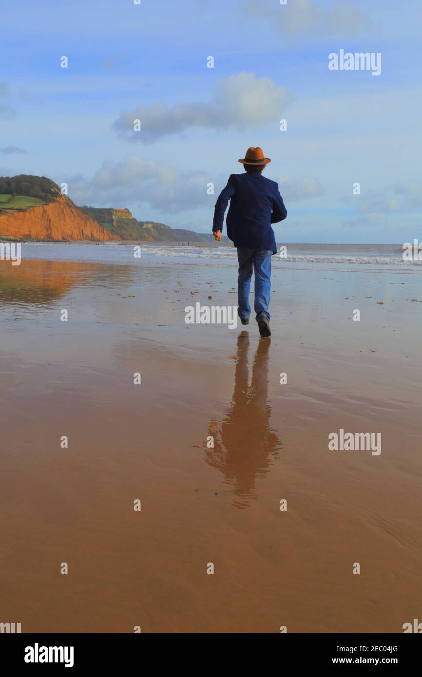 Mann mit Hut läuft am Sandstrand Stockfoto