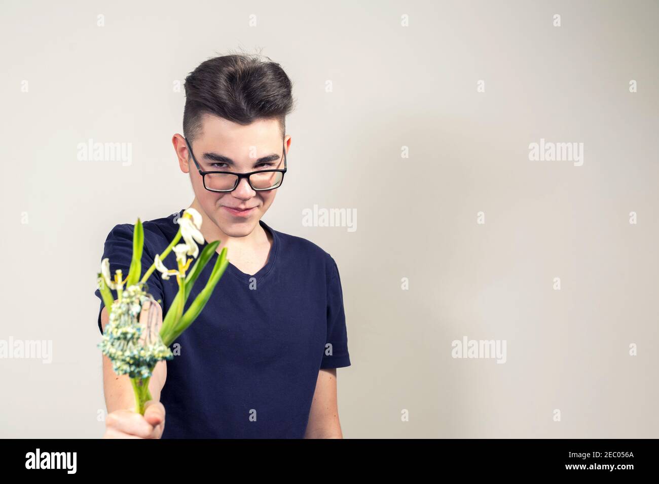 Ein bösartiger junger Mann mit Brille hält einen Strauß von verwelkt Blumen und lächelt. Das Konzept der Gier und Geiz. Konzentrieren Sie sich auf Blumen, Kerl in blu Stockfoto