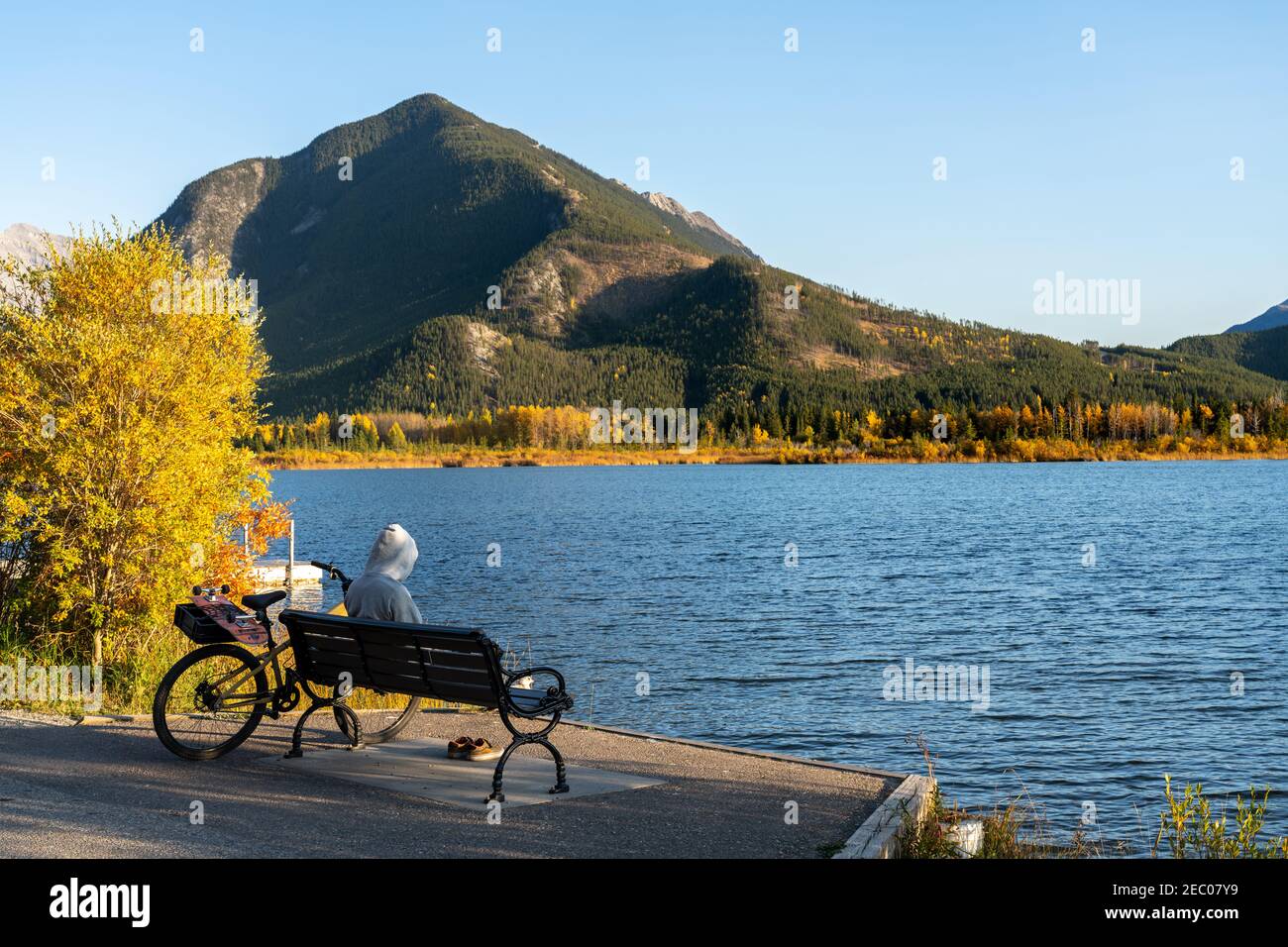 Touristen ruhen auf Holzbank, entspannen am Vermilion Lakes Seeufer im Herbst Laubsaison Sonnenuntergang Zeit. Radfahren im Banff National Park Stockfoto